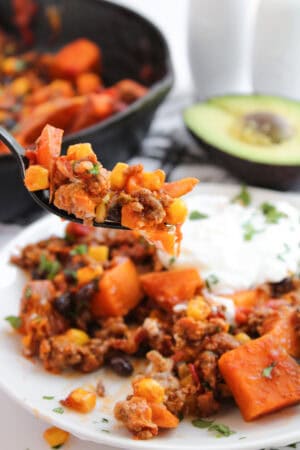 A forkful of sweet potato taco skillet with ground beef, corn, black beans, and melted cheese.