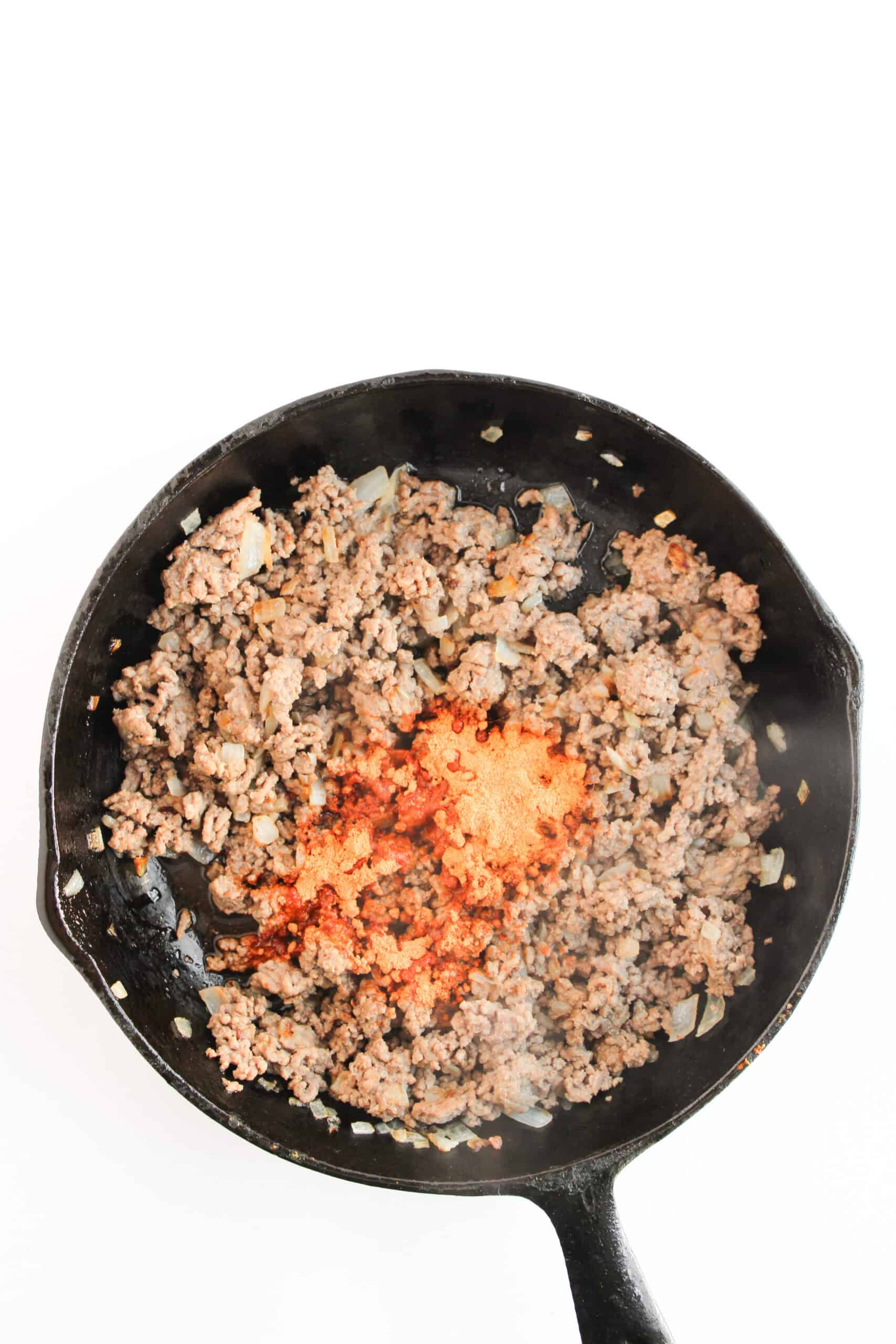 Cooked ground beef and onion with taco seasoning in a cast iron skillet.