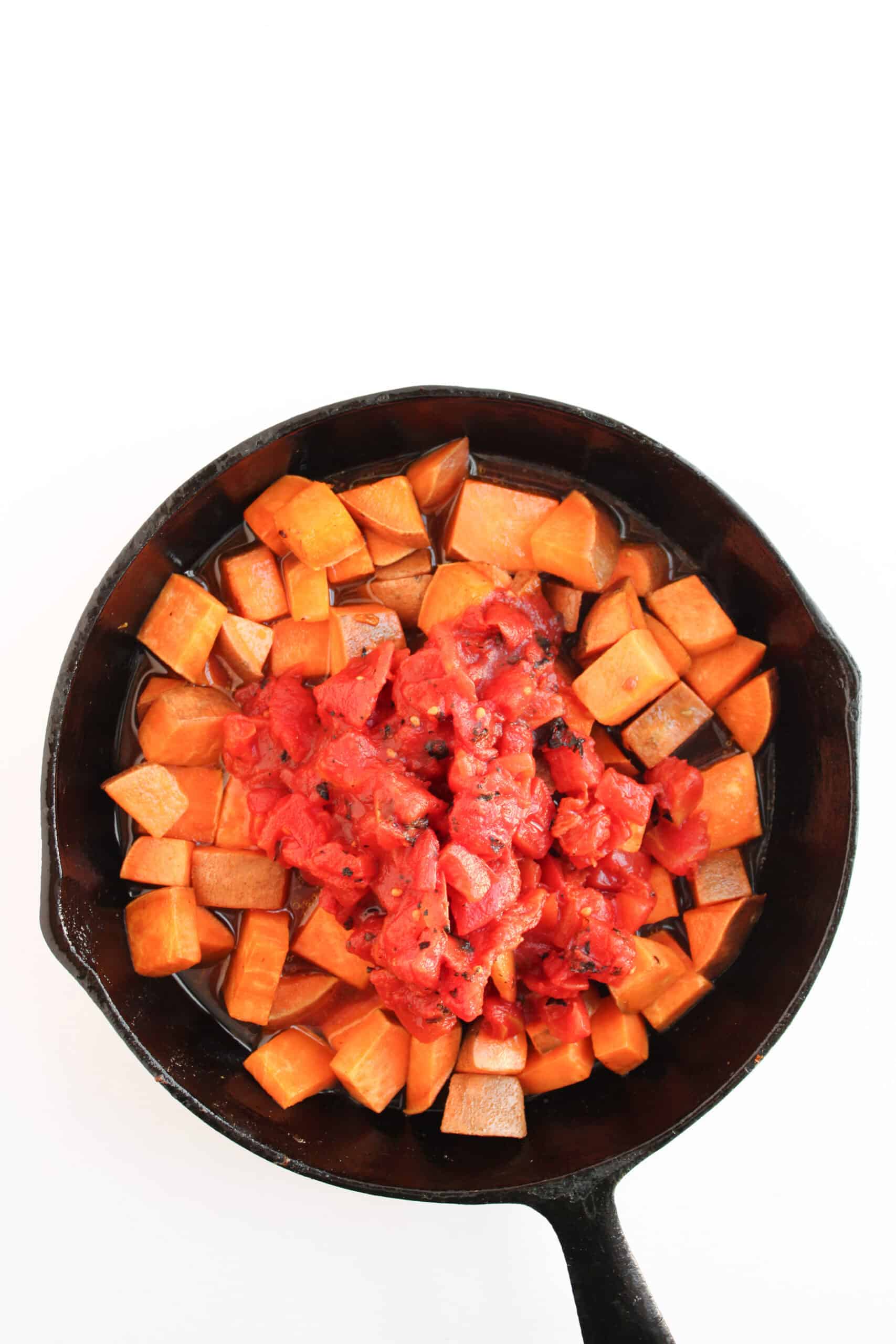 Sweet potato pieces and fire-roasted tomatoes simmering in a cast iron skillet.