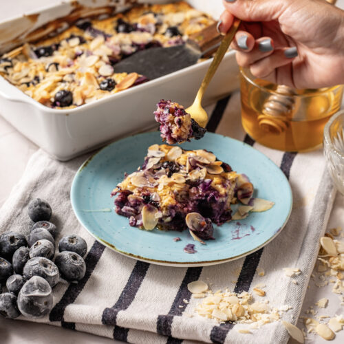 A slice of blueberry cottage cheese breakfast bake topped with sliced almonds and served with honey.