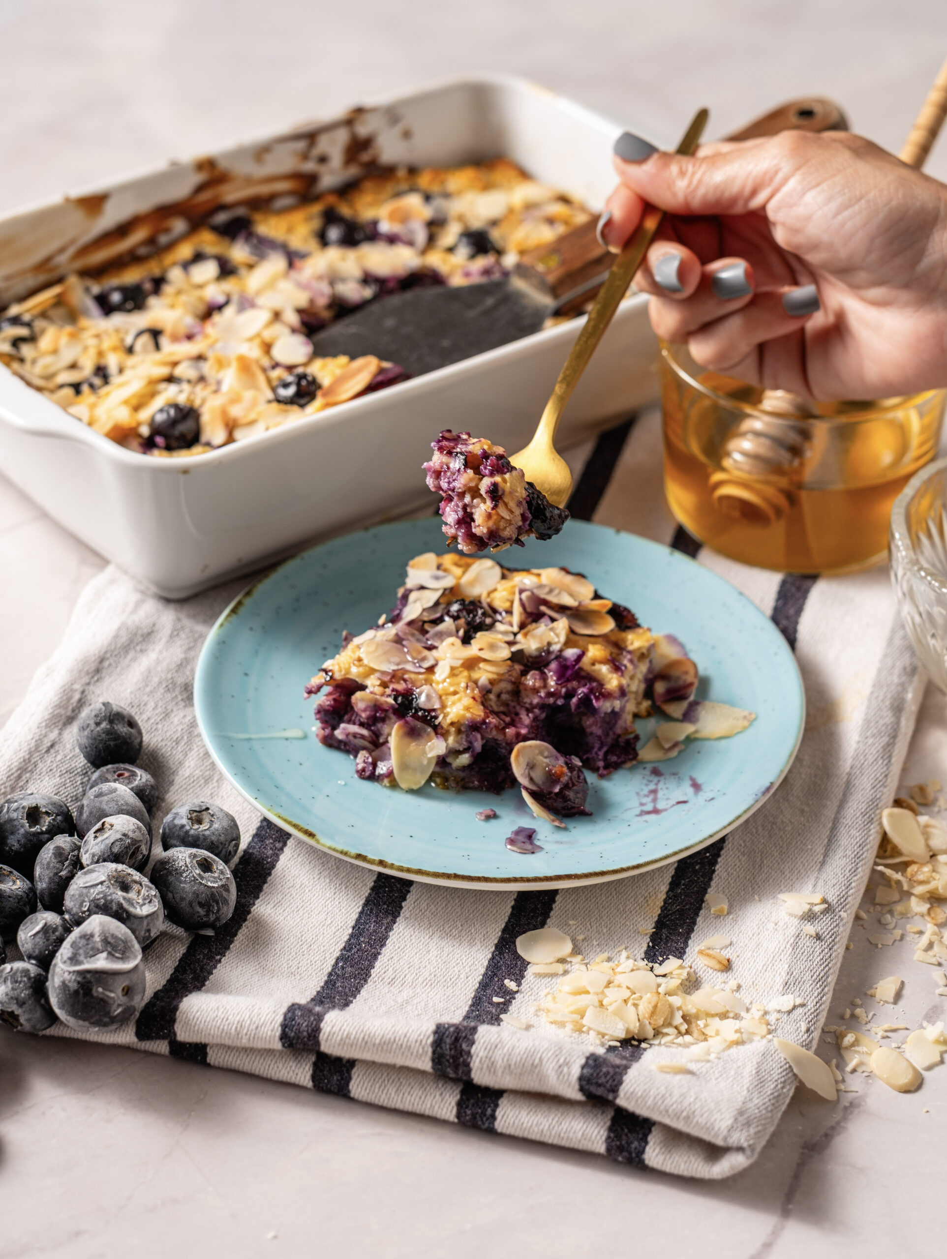 A slice of blueberry cottage cheese breakfast bake topped with sliced almonds and served with honey.