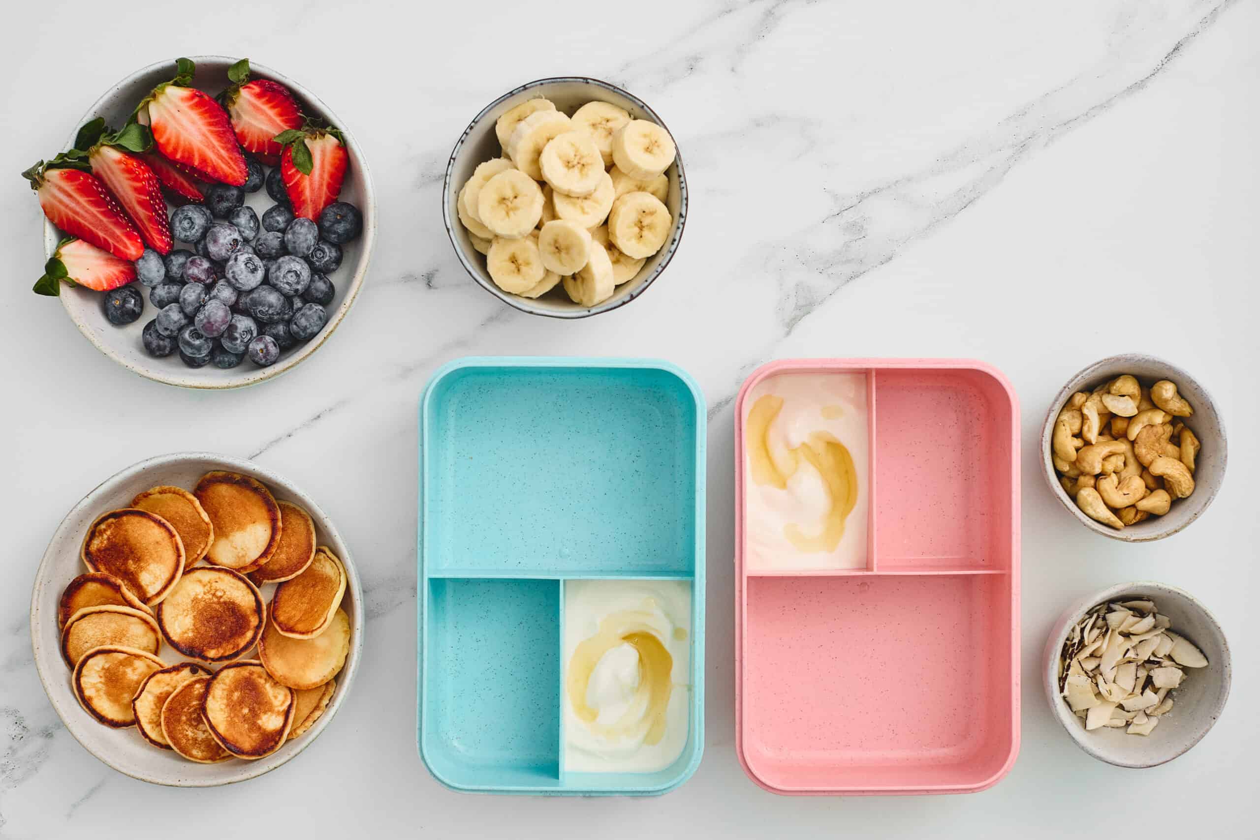 Honey drizzled over yogurt portions in two bento lunchboxes.