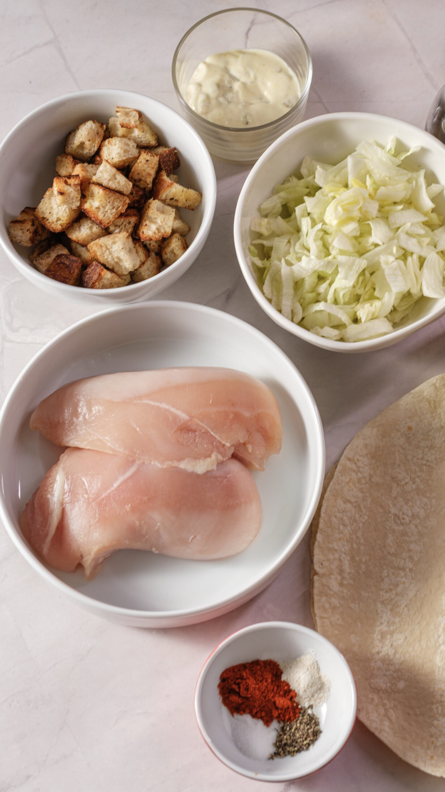 Chicken breasts, tortillas, chopped lettuce, croutons, Caesar dressing, and seasonings for chicken Caesar wraps.
