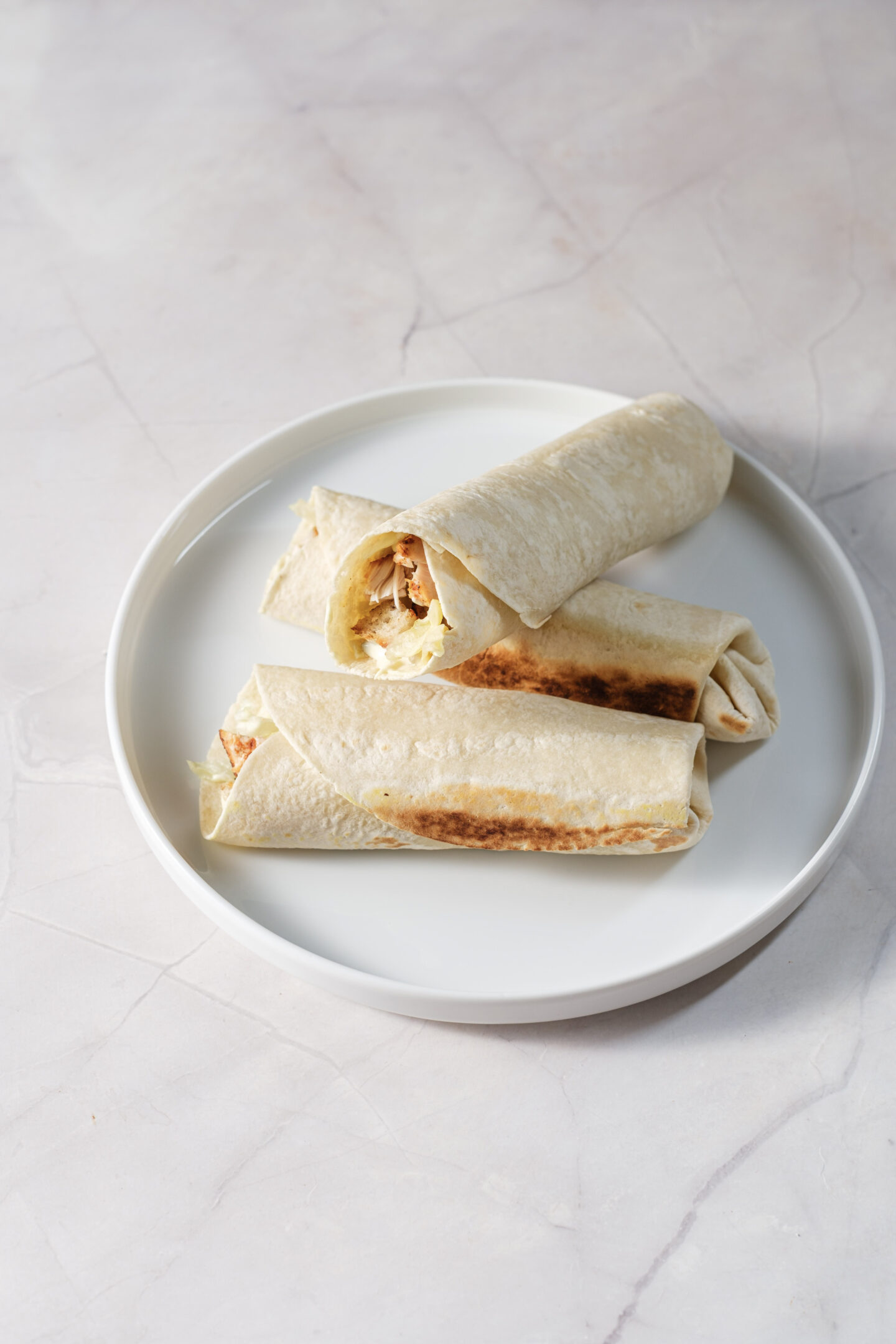 Three grilled burritos filled with meat and vegetables are arranged on a white plate, with one burrito cut open to show the filling—perfect inspiration if you're craving Easy Chicken Wraps or looking to try a homemade Chicken Caesar Wraps recipe.