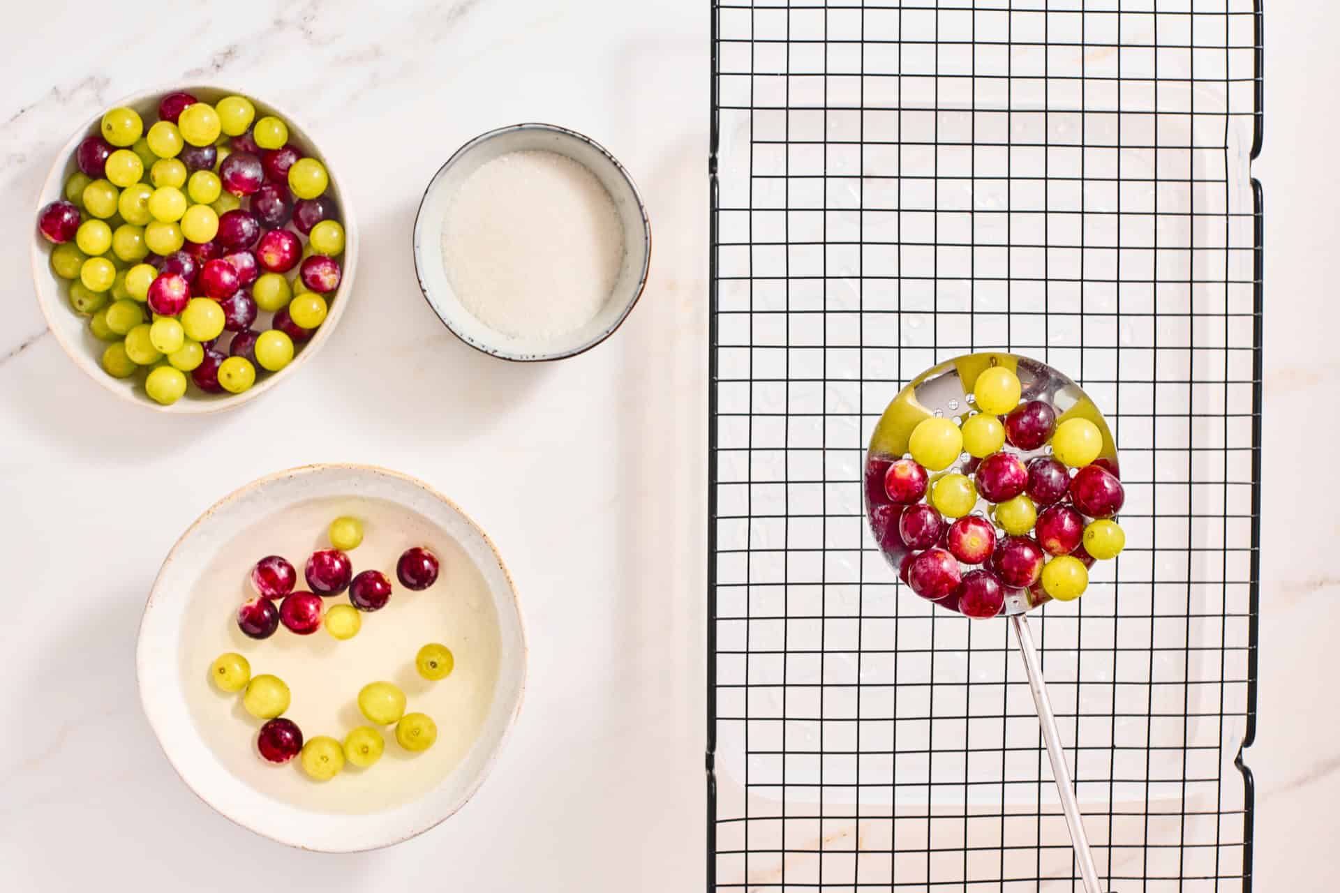 Syrup coated grapes lifted with a slotted spoon toward a wire rack.