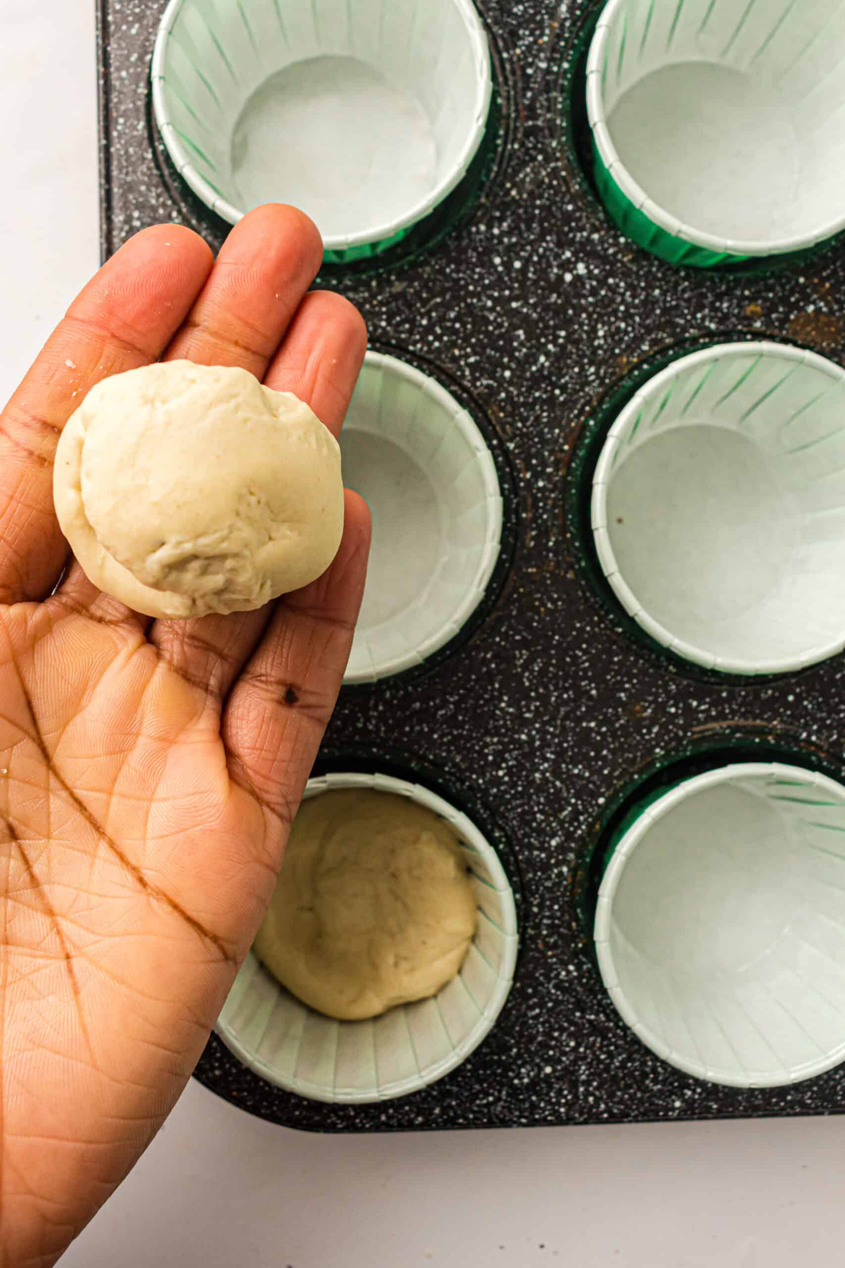 A portion of pizza dough held above a prepared muffin tin.