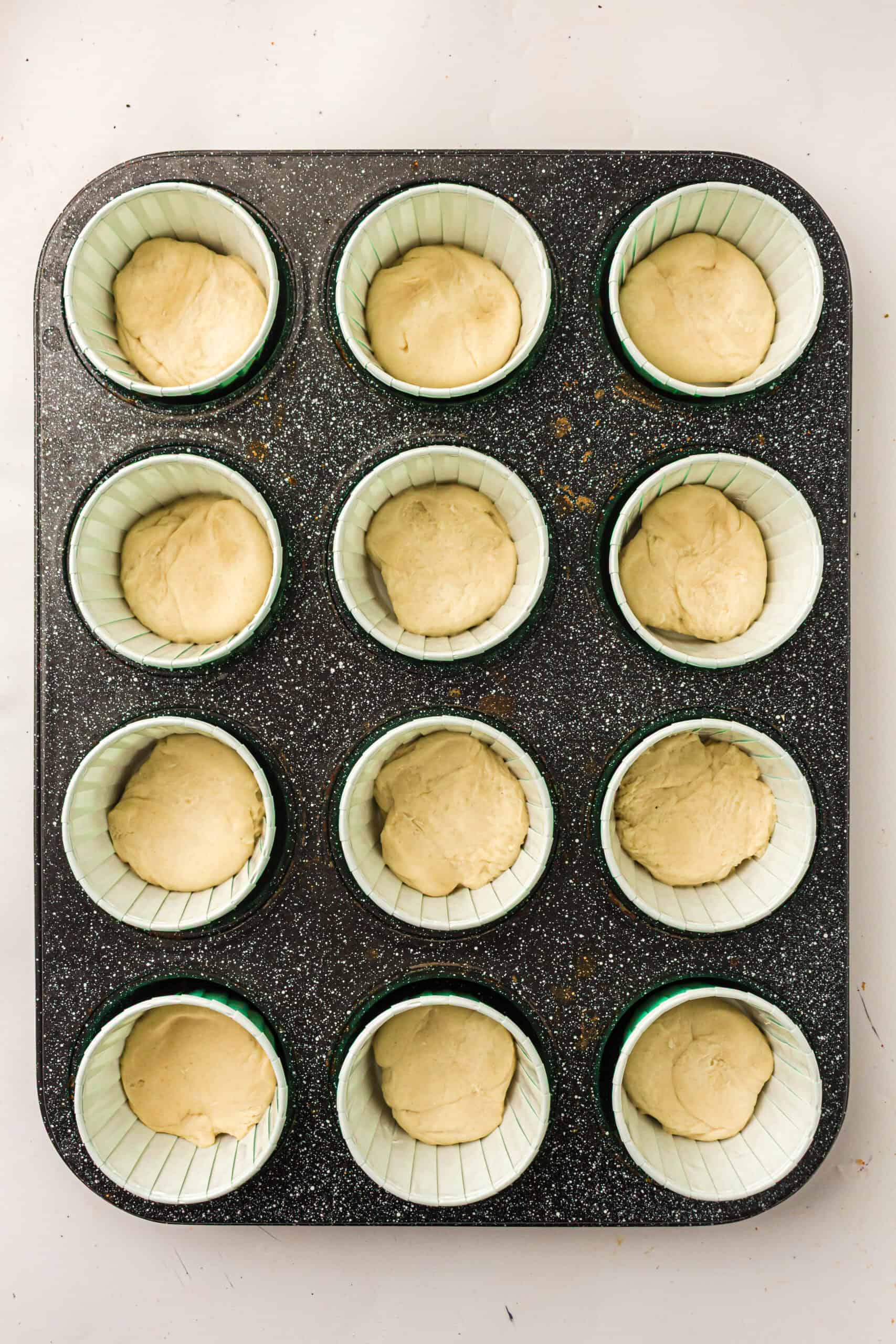 Twelve portions of pizza dough arranged in muffin cups.