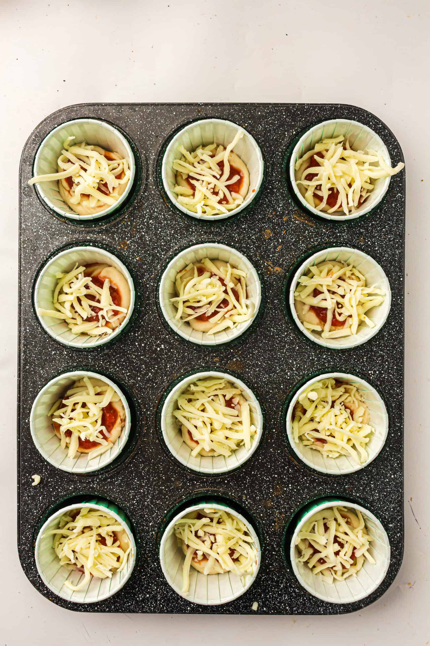 Pizza dough cups topped with sauce and shredded mozzarella.