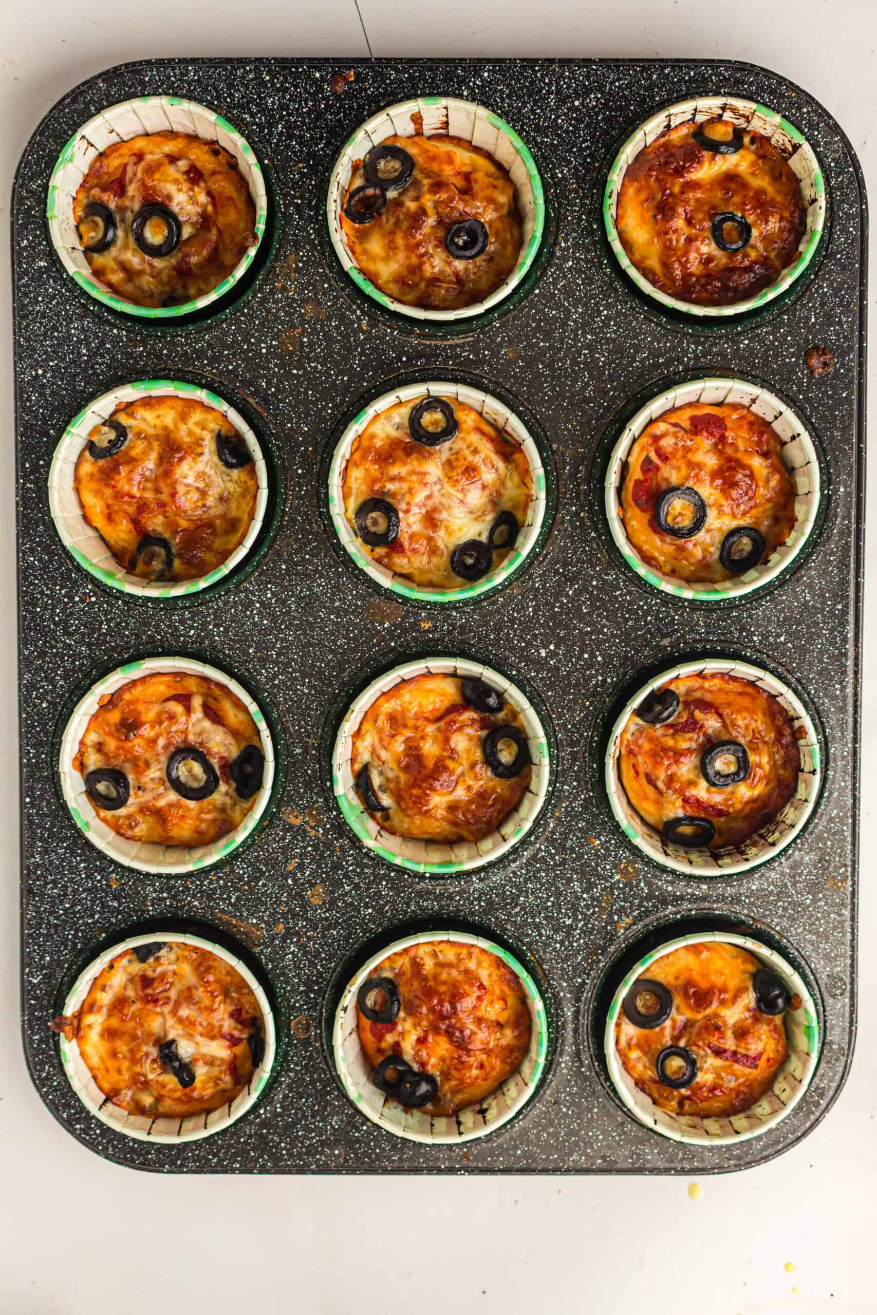 Baked pizza muffins with golden mozzarella and black olives in a muffin tin.