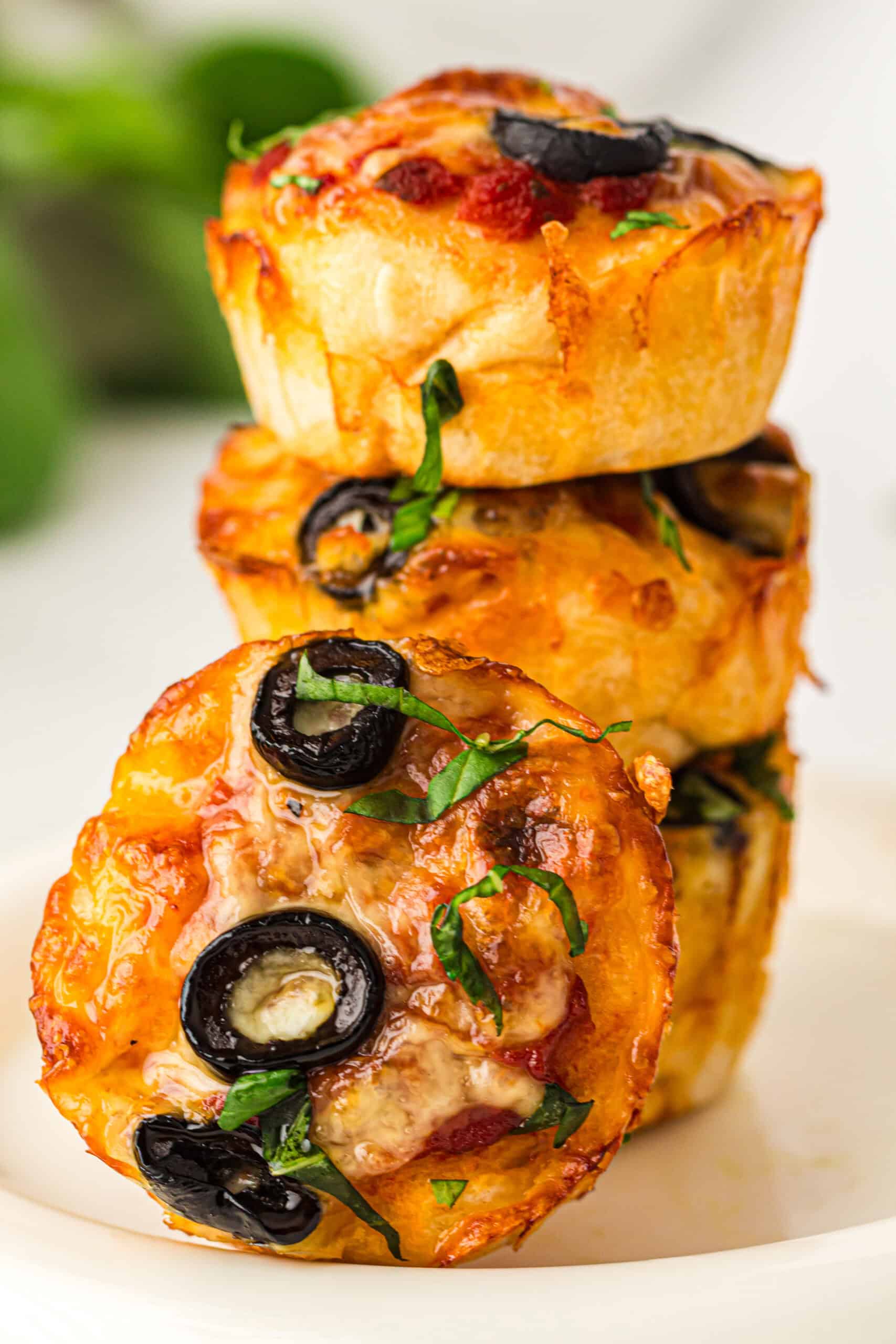 Close-up of stacked pizza muffins topped with melted cheese, black olives, and fresh basil.