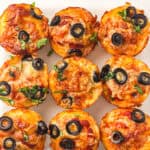 Overhead view of baked lunchbox pizza muffins with mozzarella, black olives, and fresh basil.