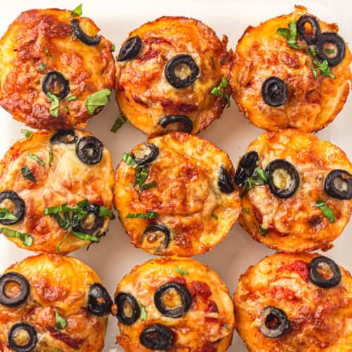 Overhead view of baked lunchbox pizza muffins with mozzarella, black olives, and fresh basil.
