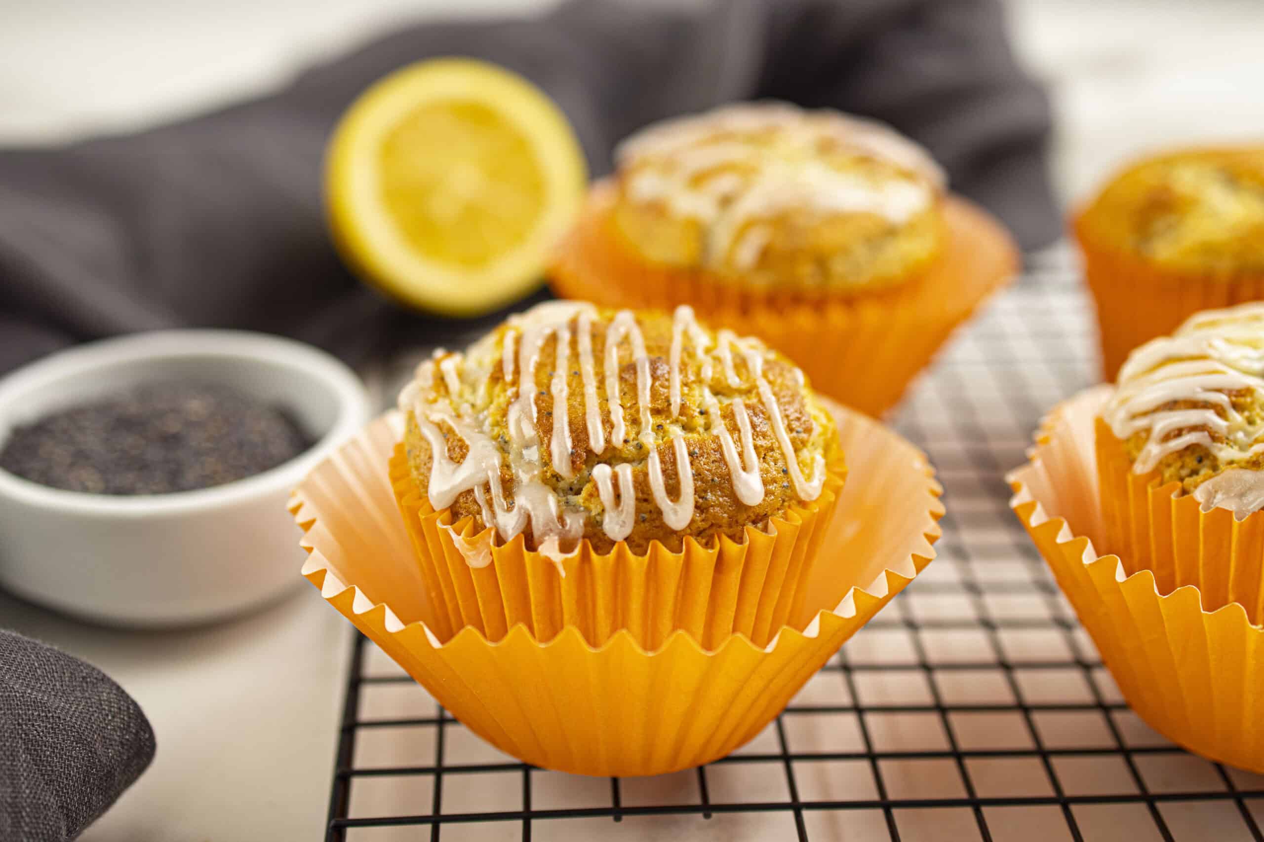 Glazed Greek yogurt lemon poppy seed muffins on a cooling rack beside lemon and poppy seeds.