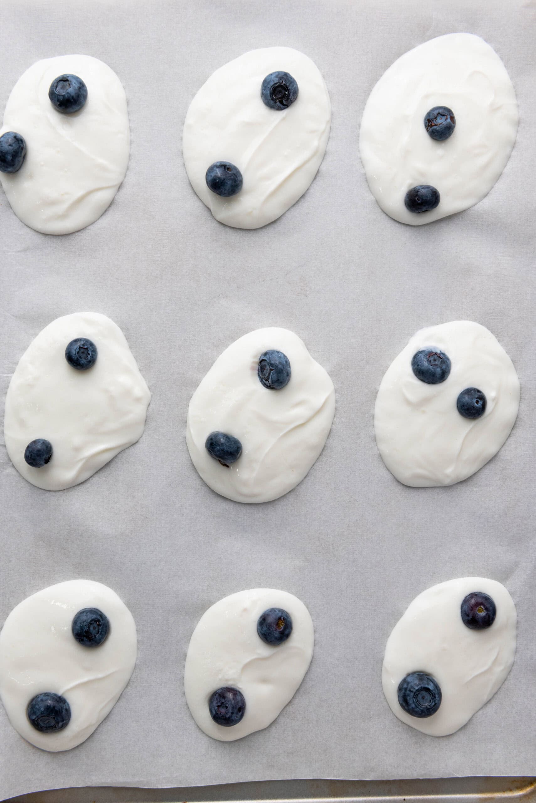 Blueberries added to Greek yogurt dollops on parchment paper.