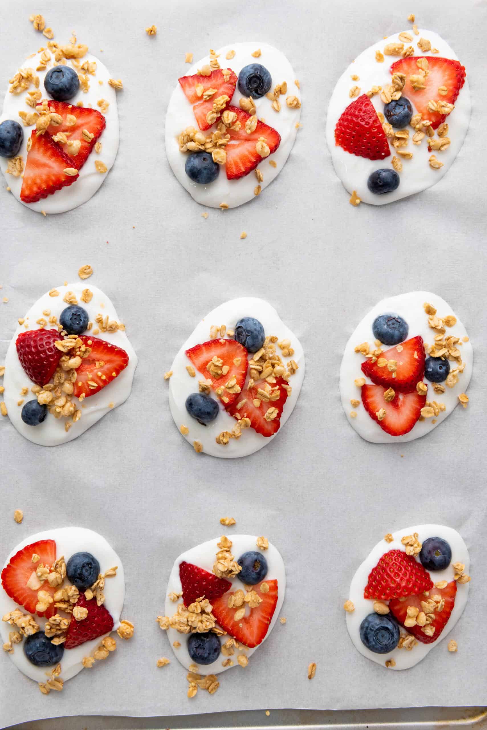 Granola sprinkled over yogurt bites topped with strawberries and blueberries.