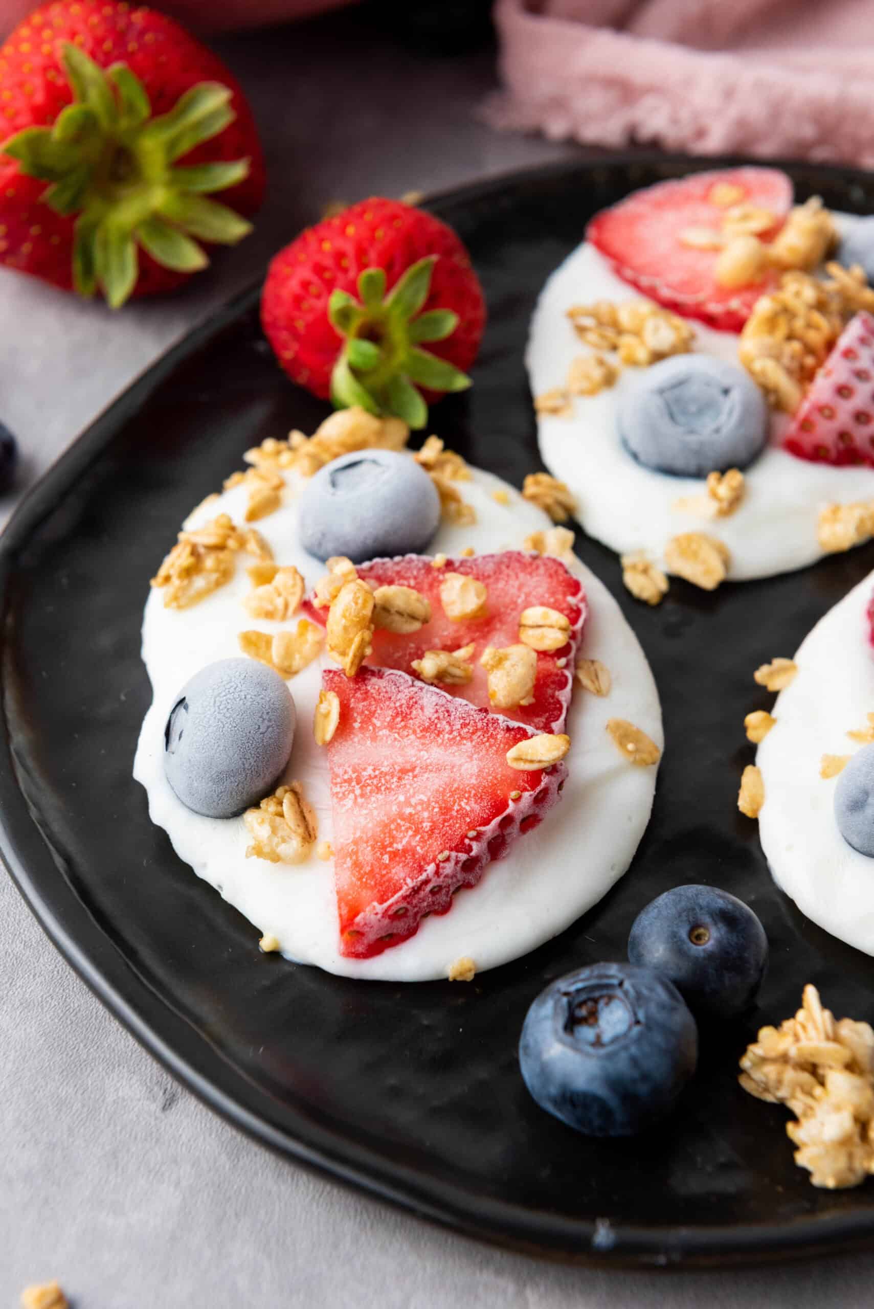 Close-up of frozen vanilla yogurt bites topped with strawberries, blueberries, and granola.