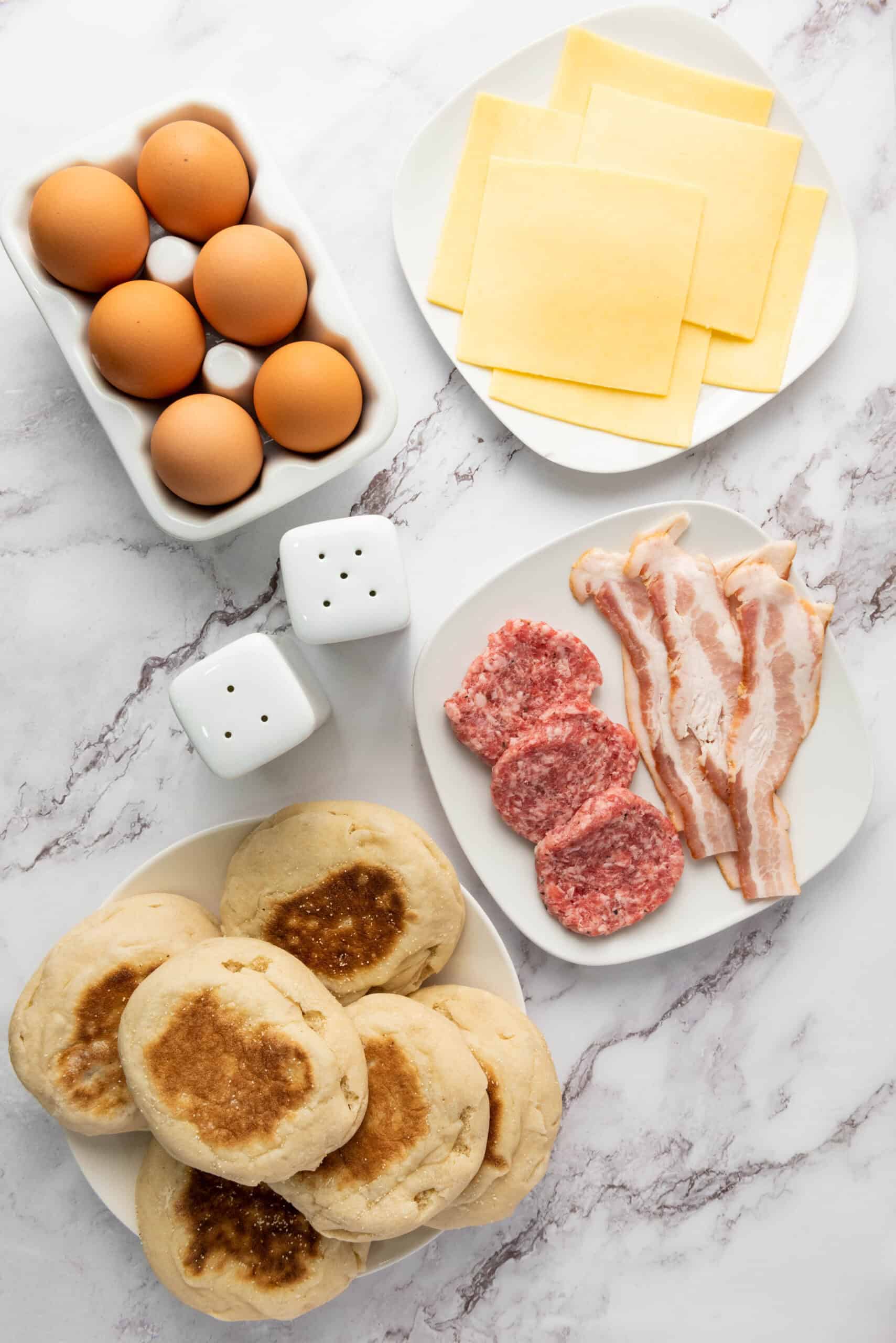 Eggs, cheese, bacon, sausage patties, and English muffins for freezer breakfast sandwiches.