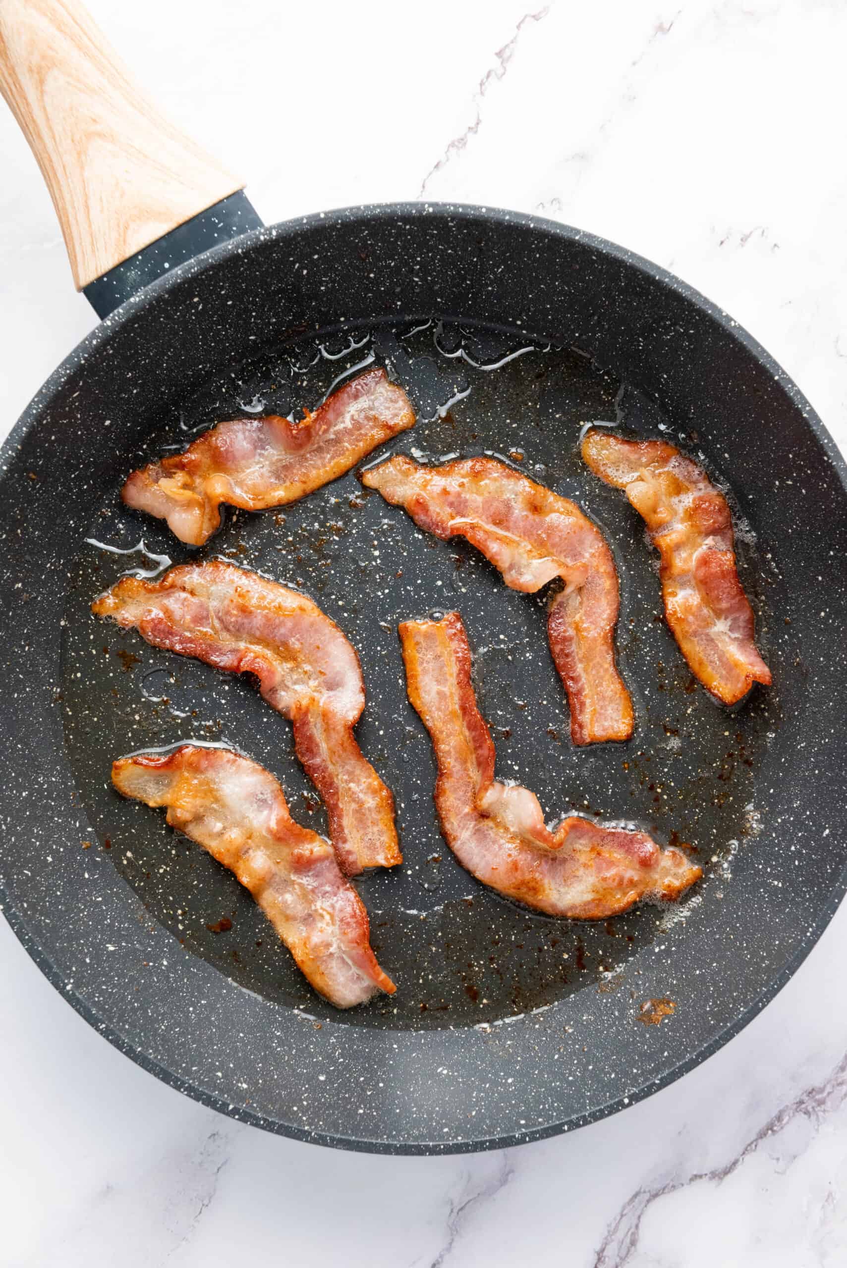 Bacon slices cooking in a skillet for breakfast sandwiches.