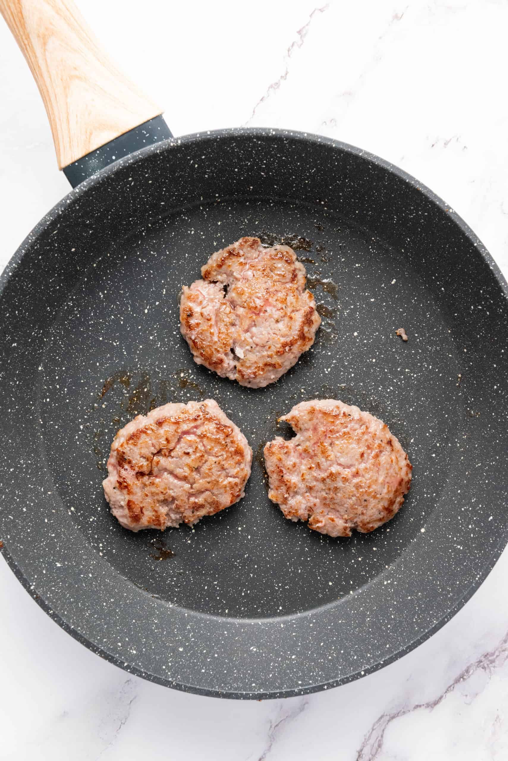 Sausage patties cooking in a skillet for breakfast sandwiches.