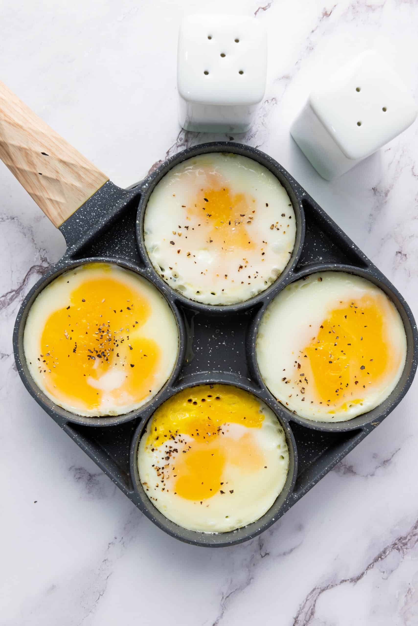 Eggs cooking in round rings and seasoned with salt and pepper.