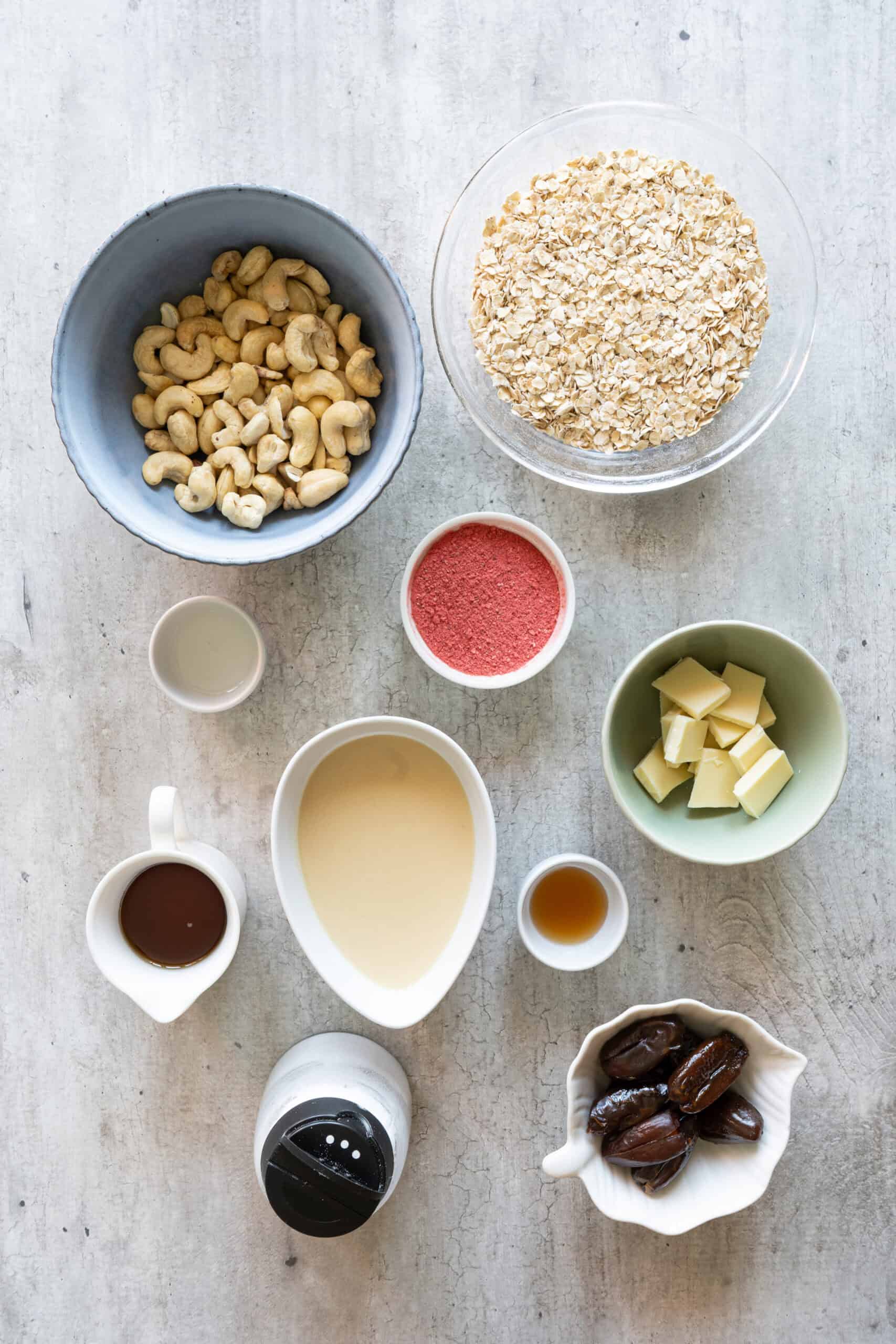 Oats, cashews, dates, almond butter, maple syrup, freeze-dried strawberries, white chocolate, vanilla, coconut oil, and salt.