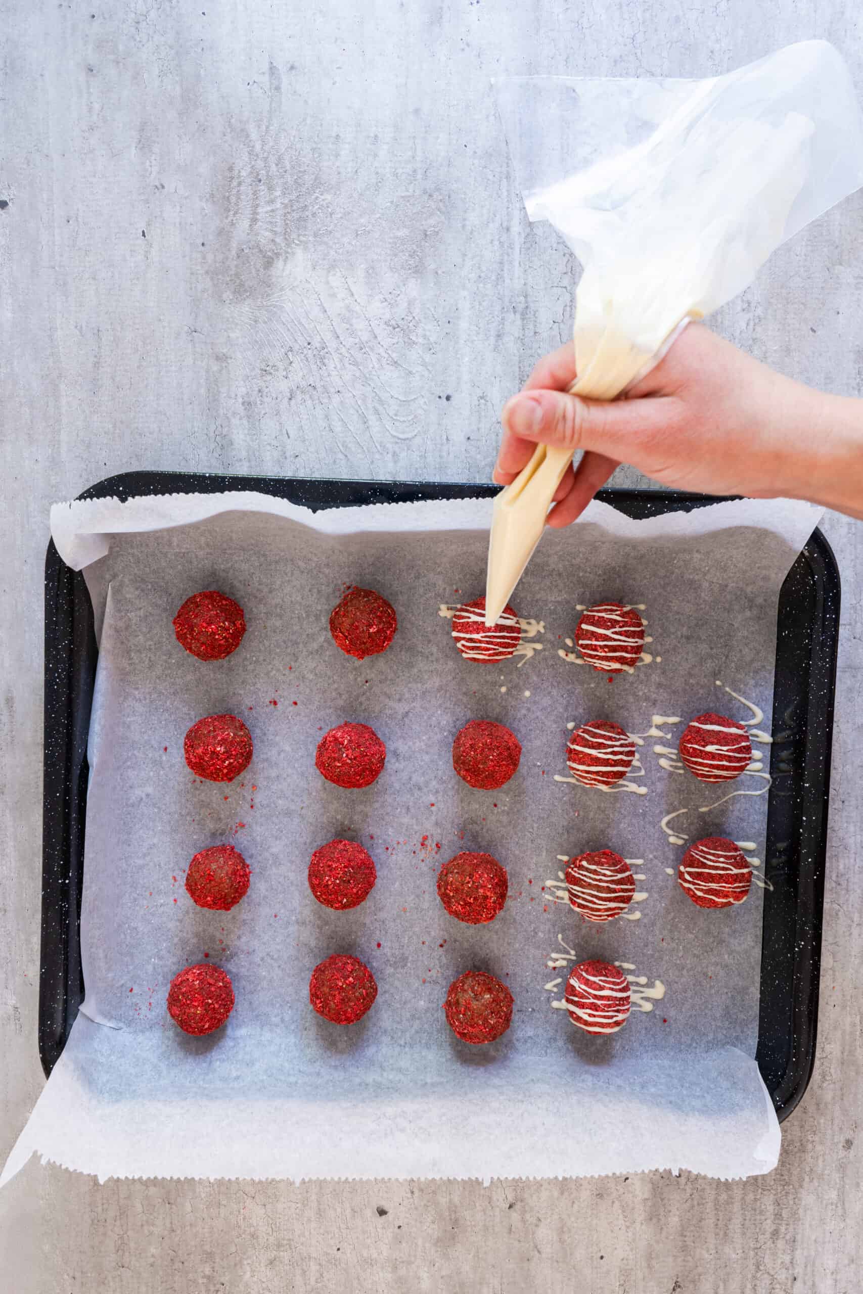 White chocolate drizzle being applied to chilled strawberry energy bites.