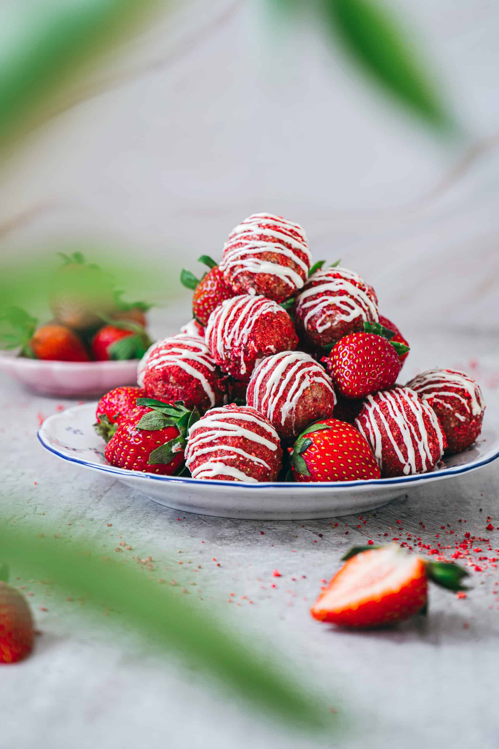 Strawberry shortcake energy bites with white chocolate drizzle arranged with fresh strawberries.