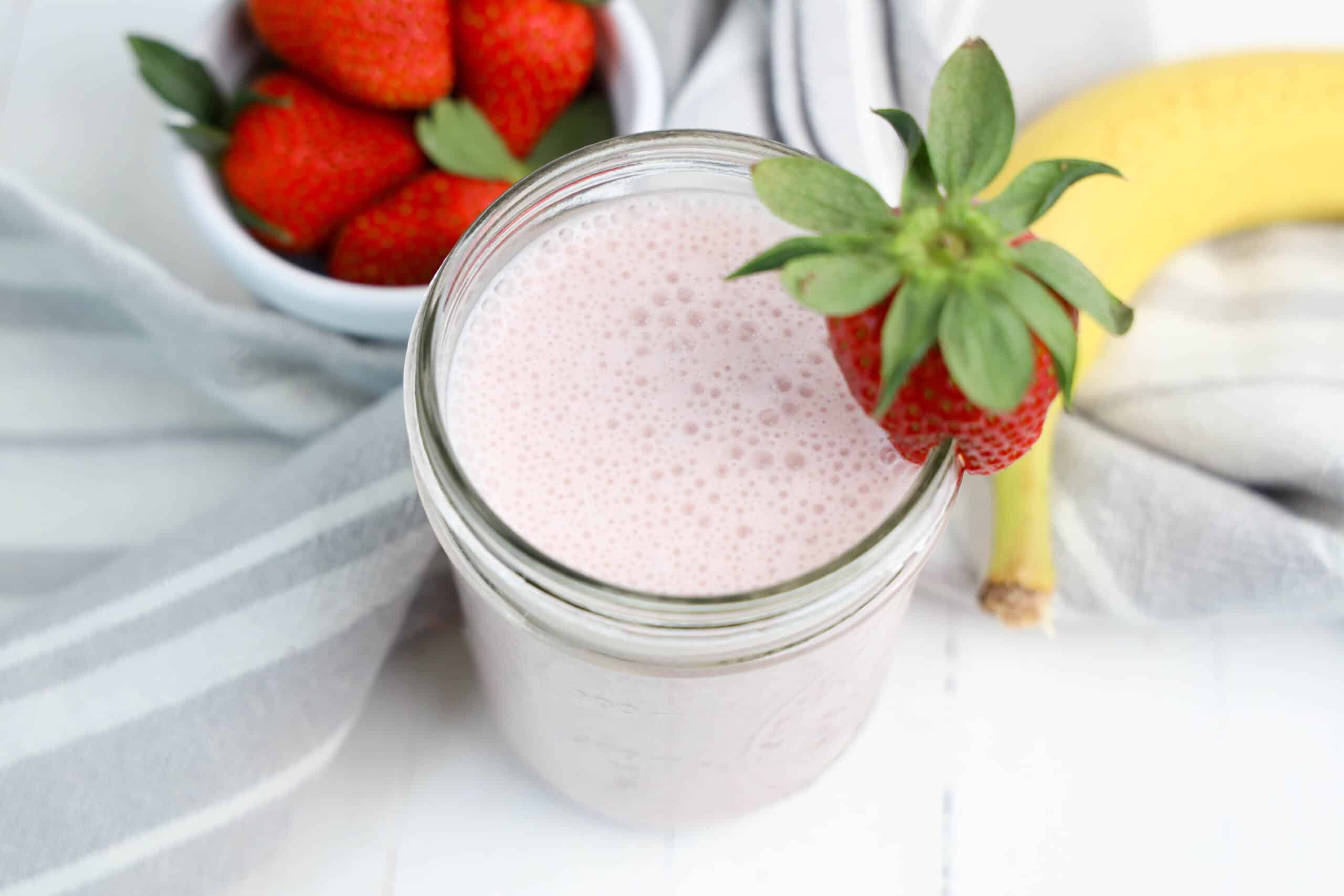 Strawberry banana smoothie garnished with a strawberry beside fresh fruit.