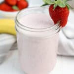 Strawberry banana smoothie in a glass jar garnished with a fresh strawberry.