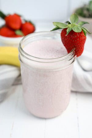 Strawberry banana smoothie in a glass jar garnished with a fresh strawberry.