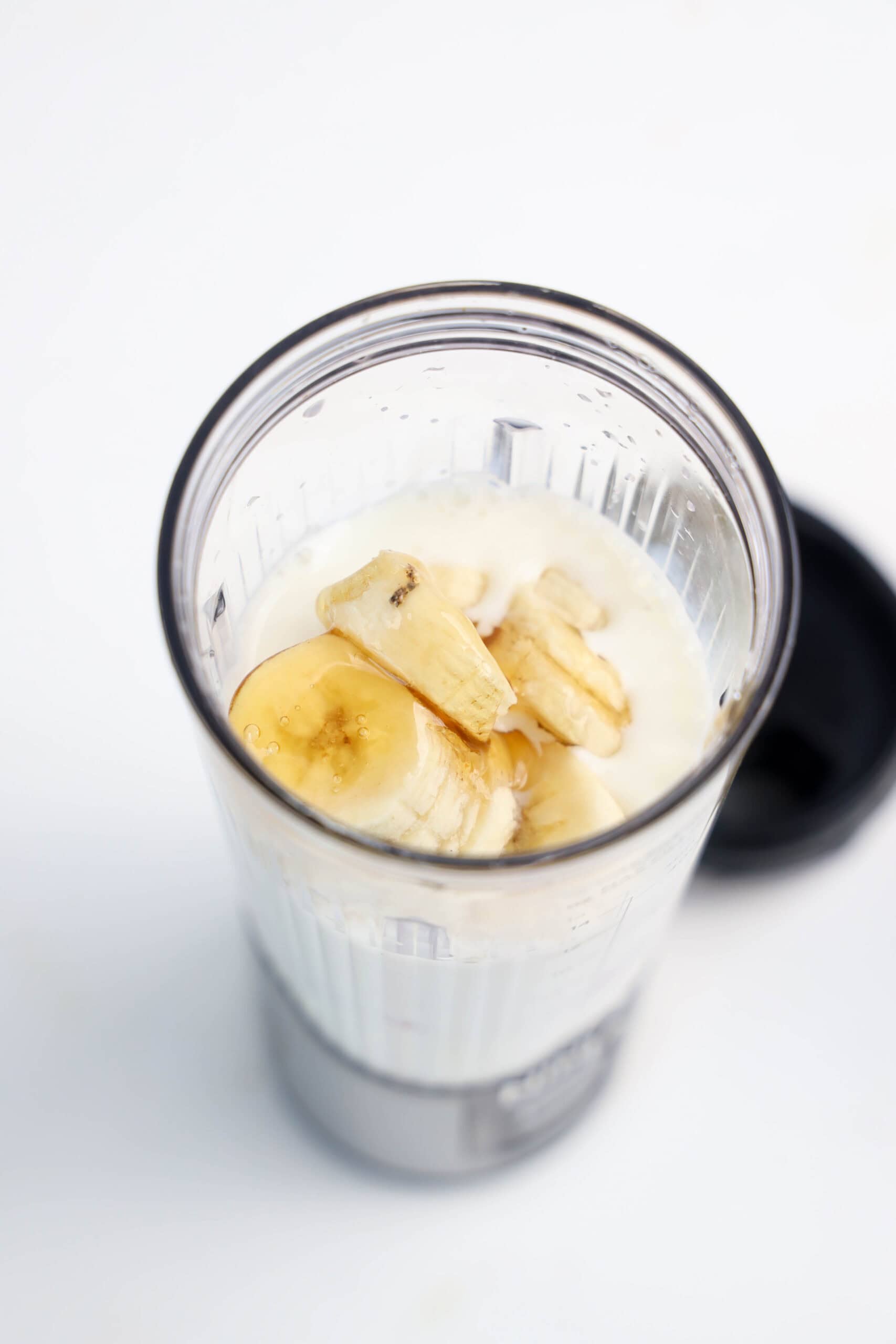 Sliced banana added to milk in a personal blender cup.