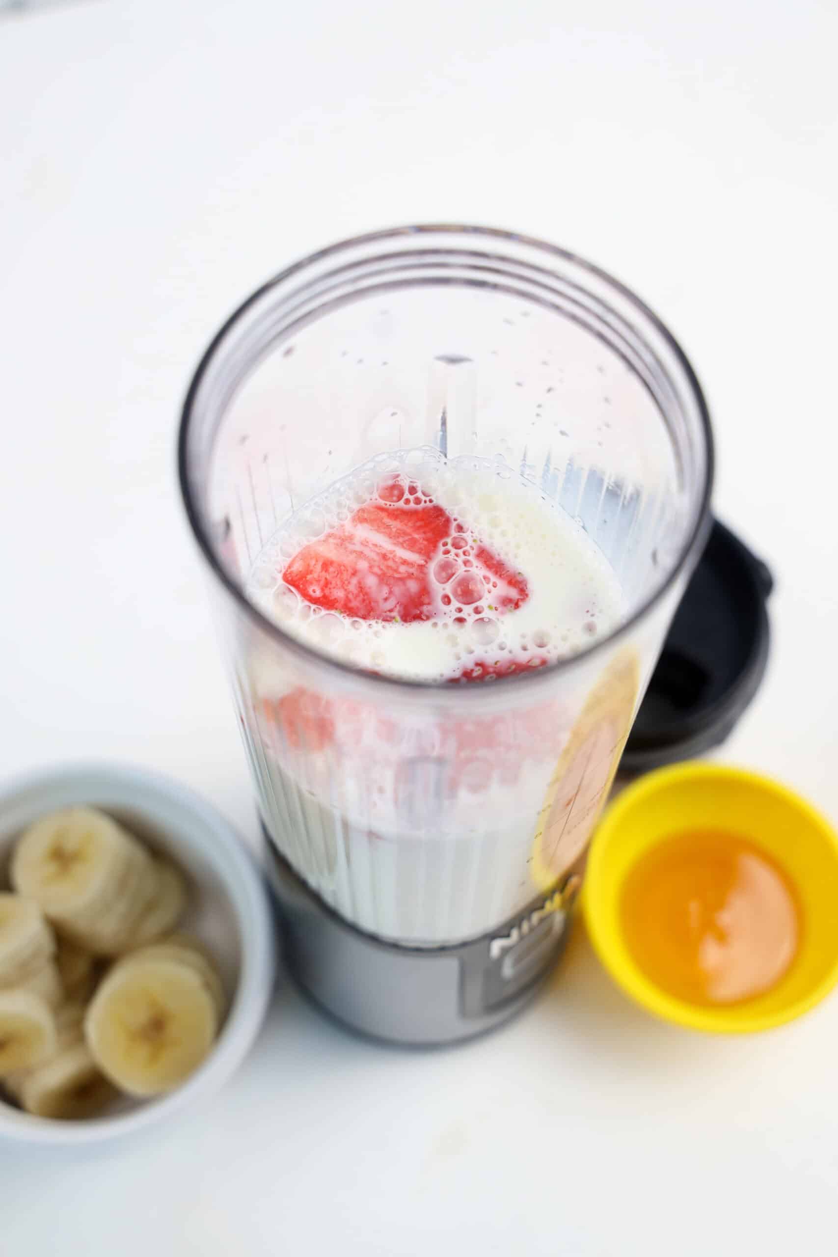 Sliced strawberries added to milk and banana in a personal blender.