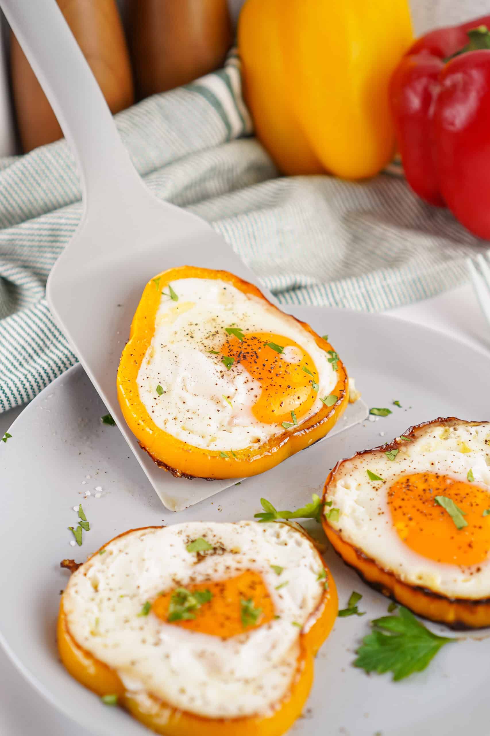 Bell pepper egg rings being served from a plate with a spatula.
