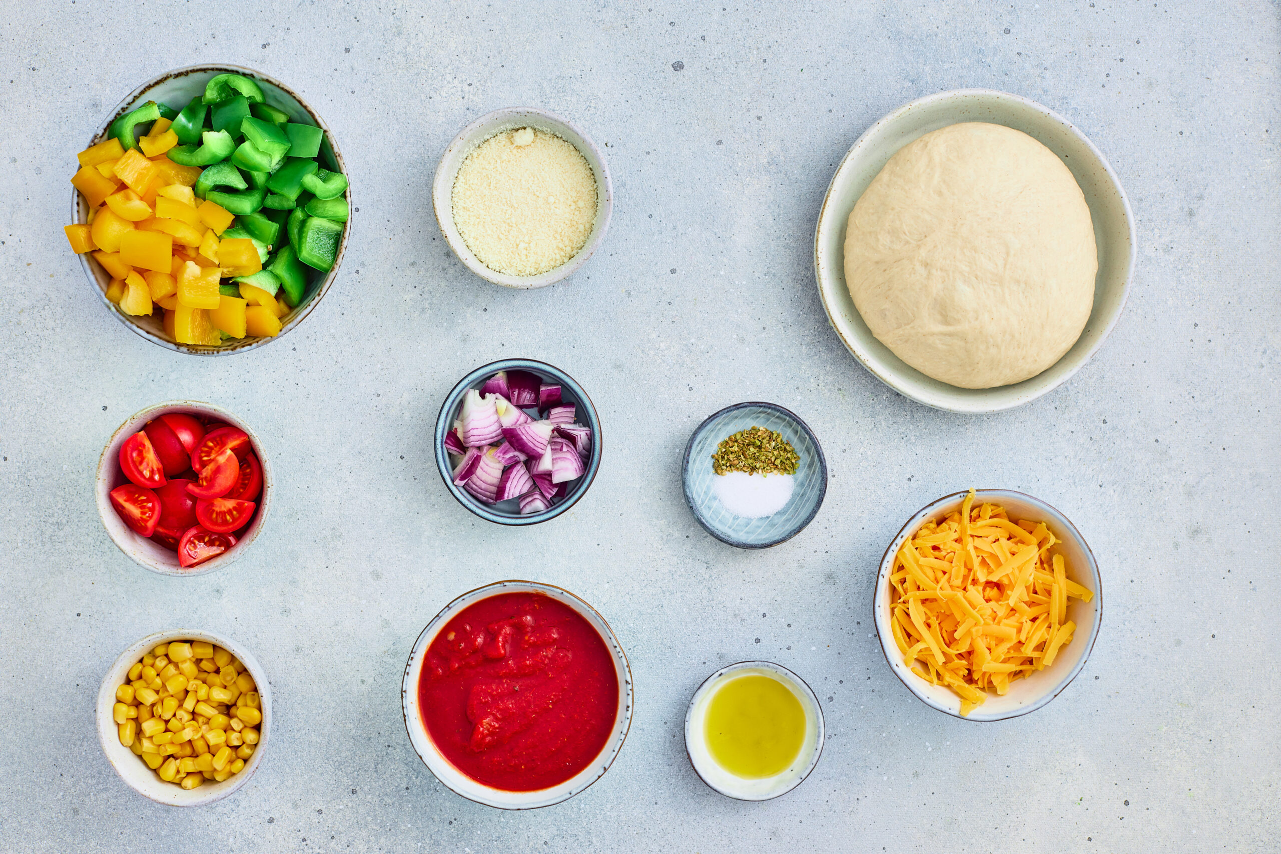 Pizza dough, tomato sauce, parmesan, cheddar, tomatoes, peppers, corn, red onion, olive oil, oregano, and salt.