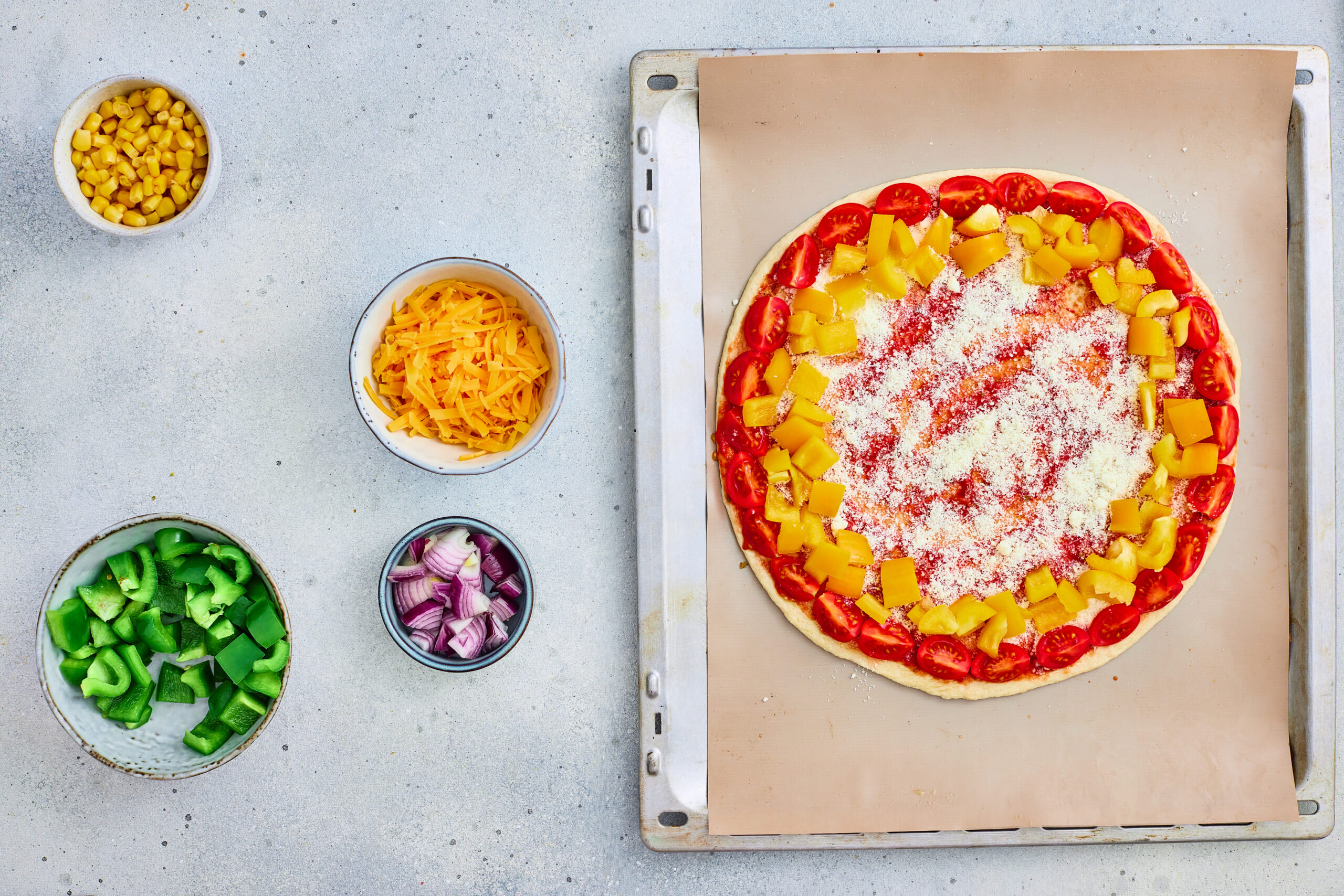 Cherry tomatoes and yellow bell pepper arranged in outer rings on pizza dough.