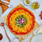 Baked rainbow wheel veggie pizza topped with colorful vegetable rings.