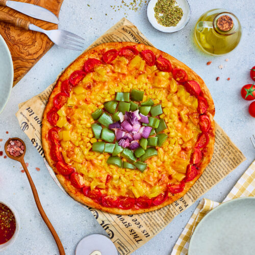 Baked rainbow wheel veggie pizza topped with colorful vegetable rings.