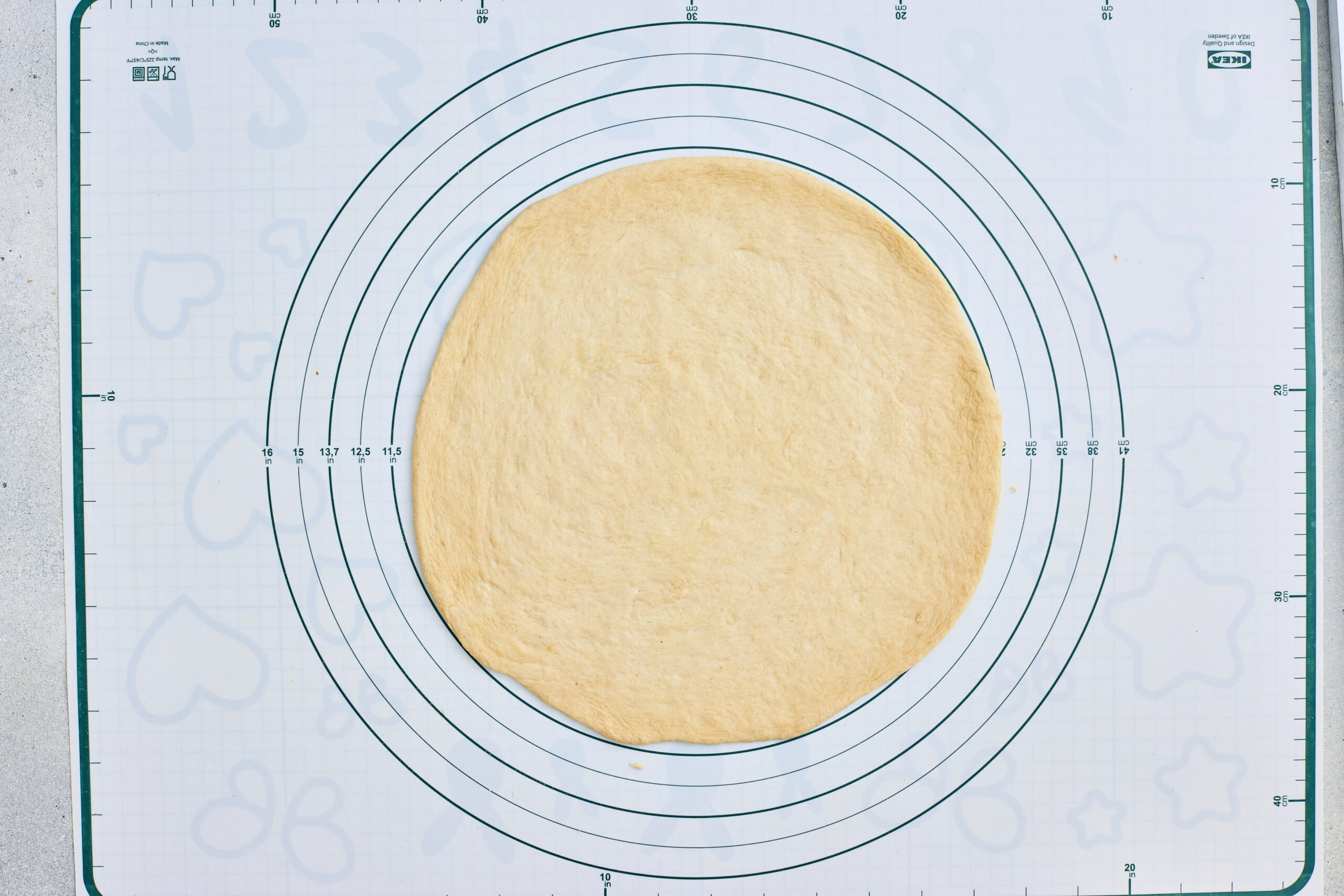 Pizza dough rolled into a large round on a pastry mat.