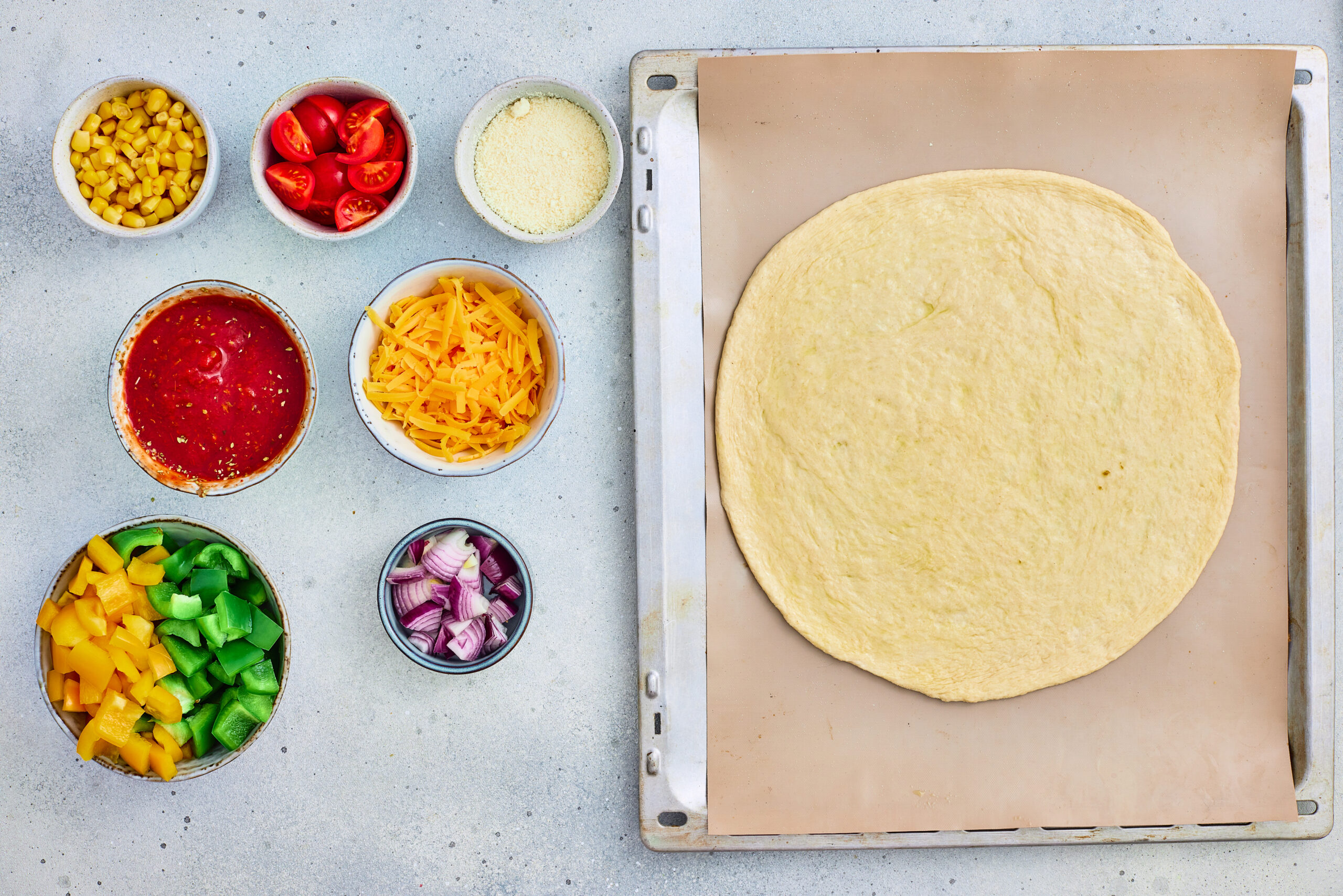 Rolled pizza dough with olive oil and seasoned tomato sauce ready to spread.