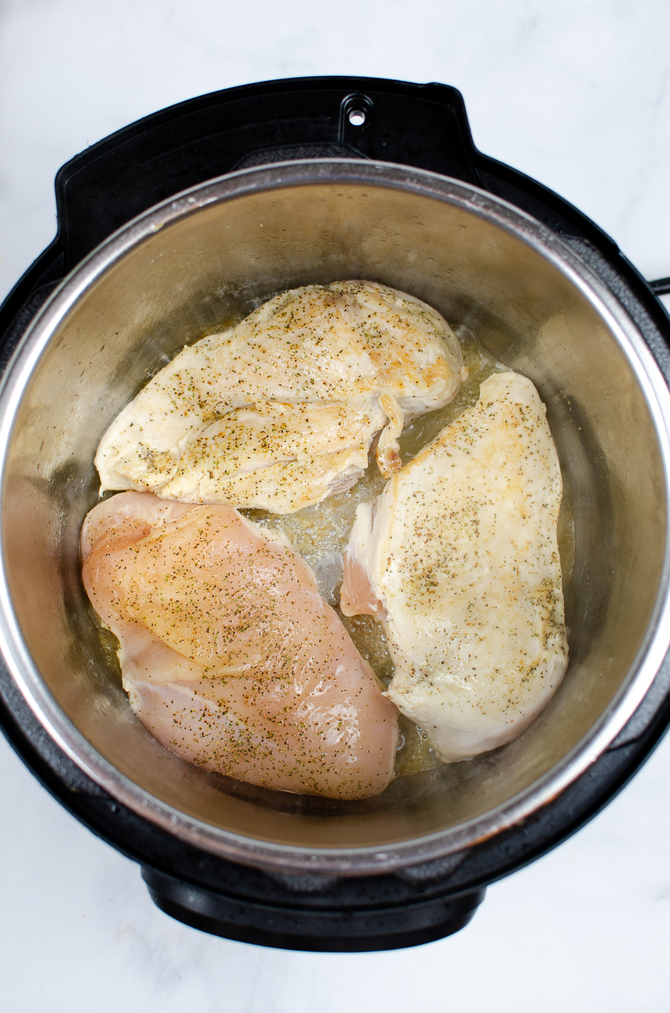 Seasoned chicken breasts browning in olive oil in an Instant Pot.
