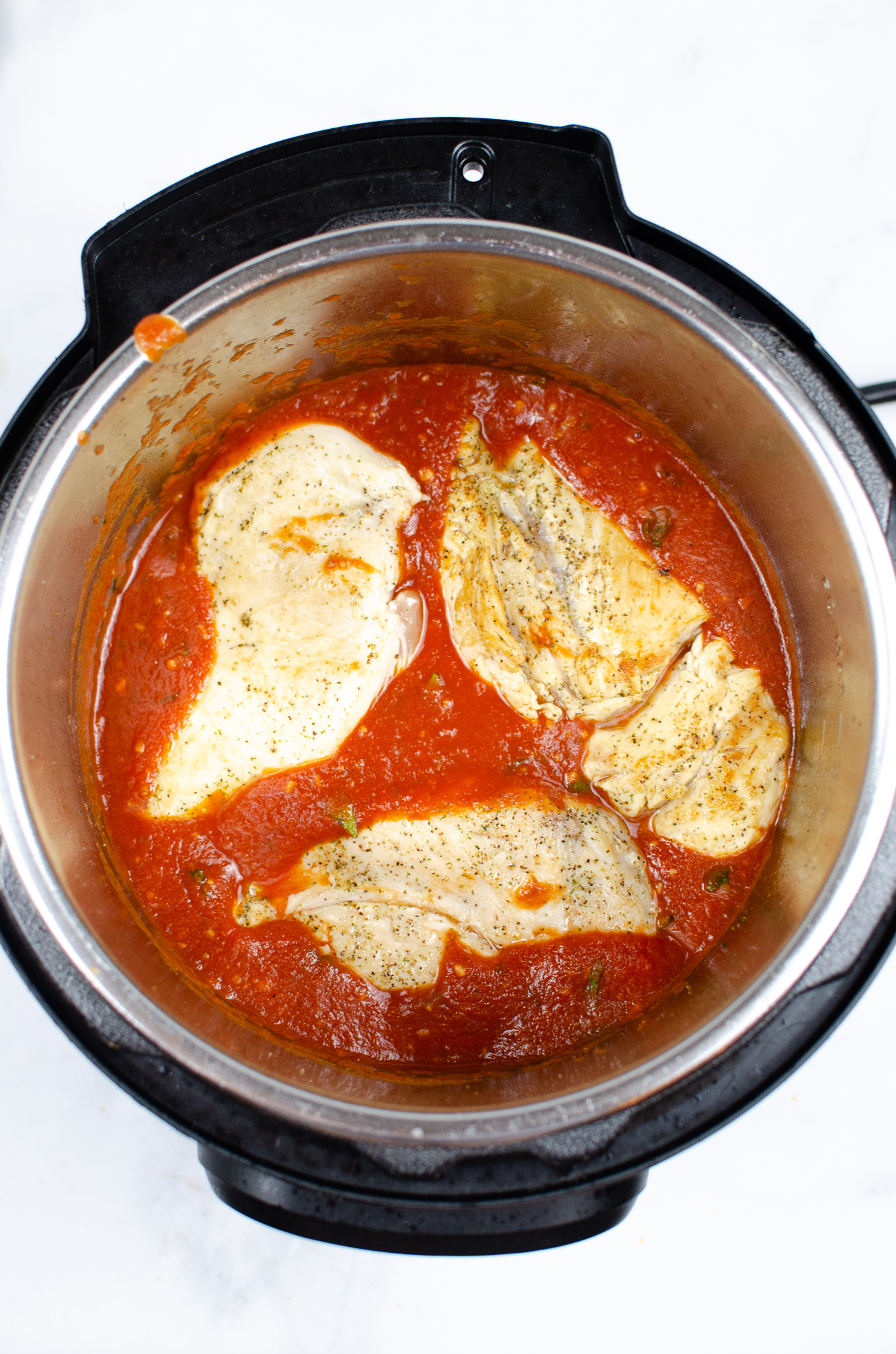 Browned chicken breasts nestled in marinara sauce in an Instant Pot.