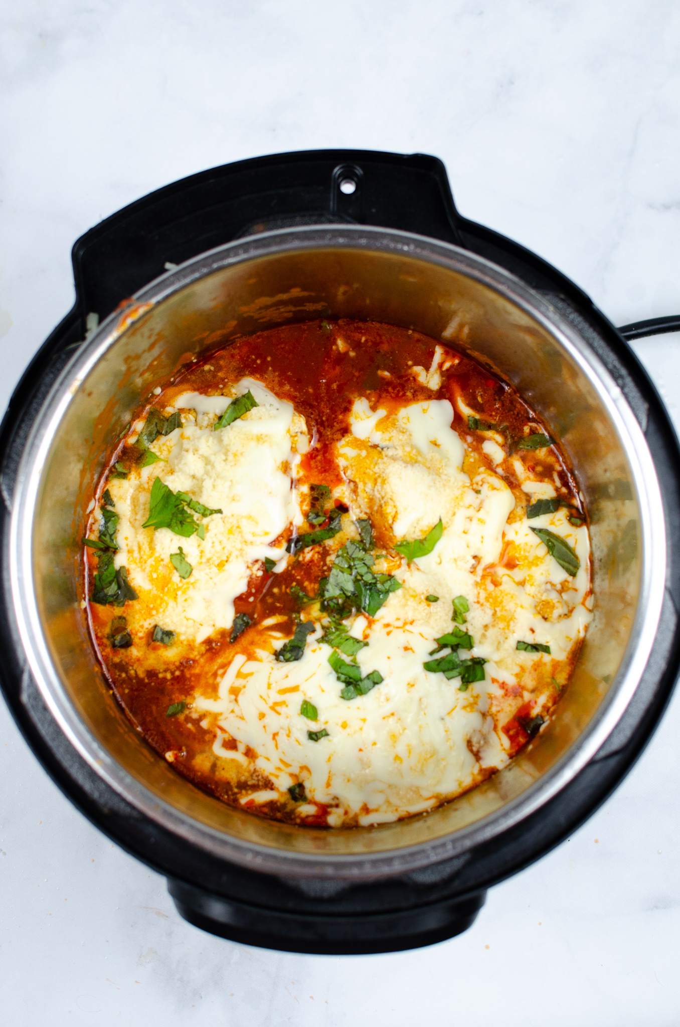 Instant Pot chicken Parmesan with melted mozzarella, Parmesan, and basil.