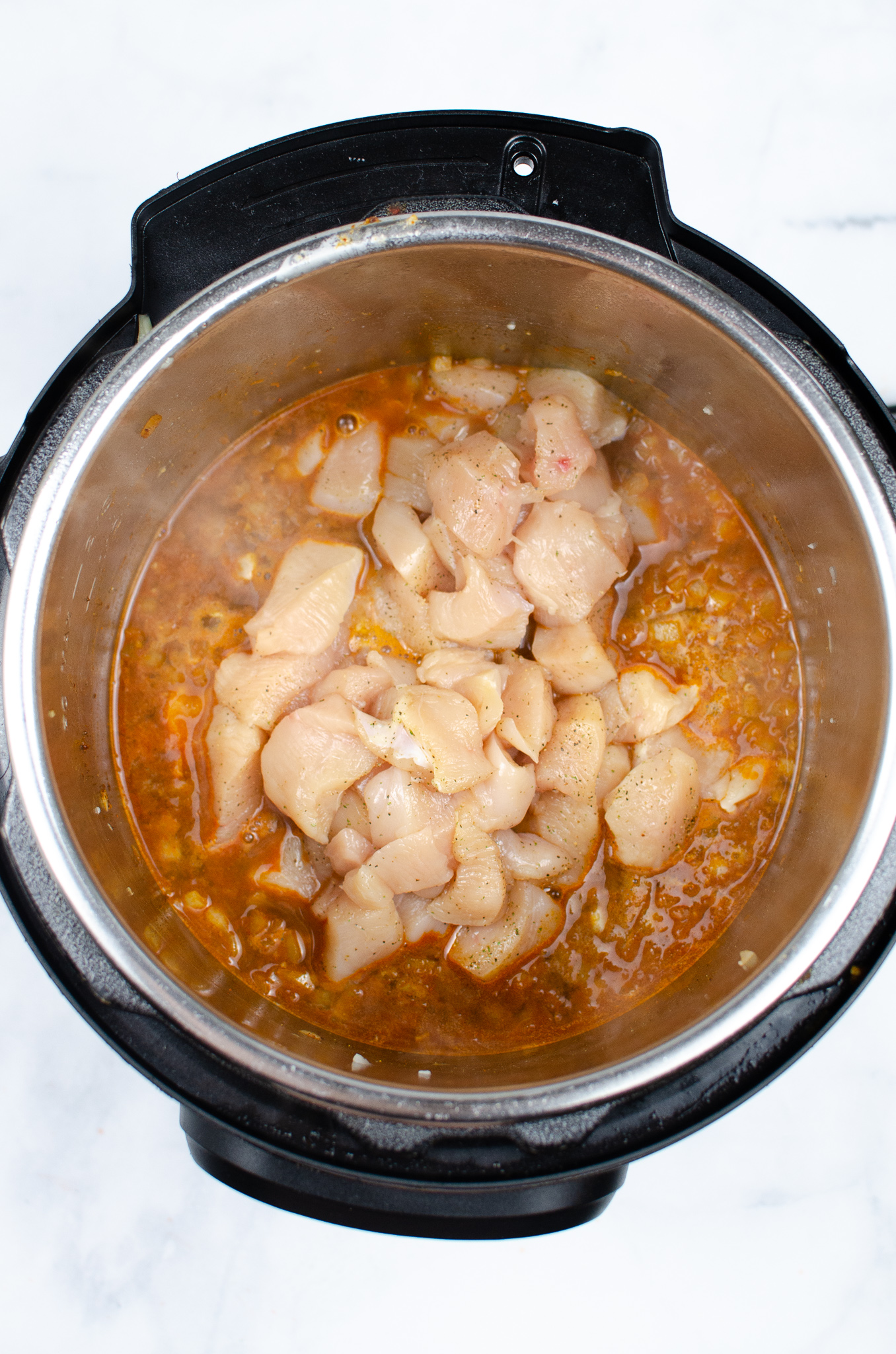 Seasoned chicken pieces added to broth and seasonings in an Instant Pot.