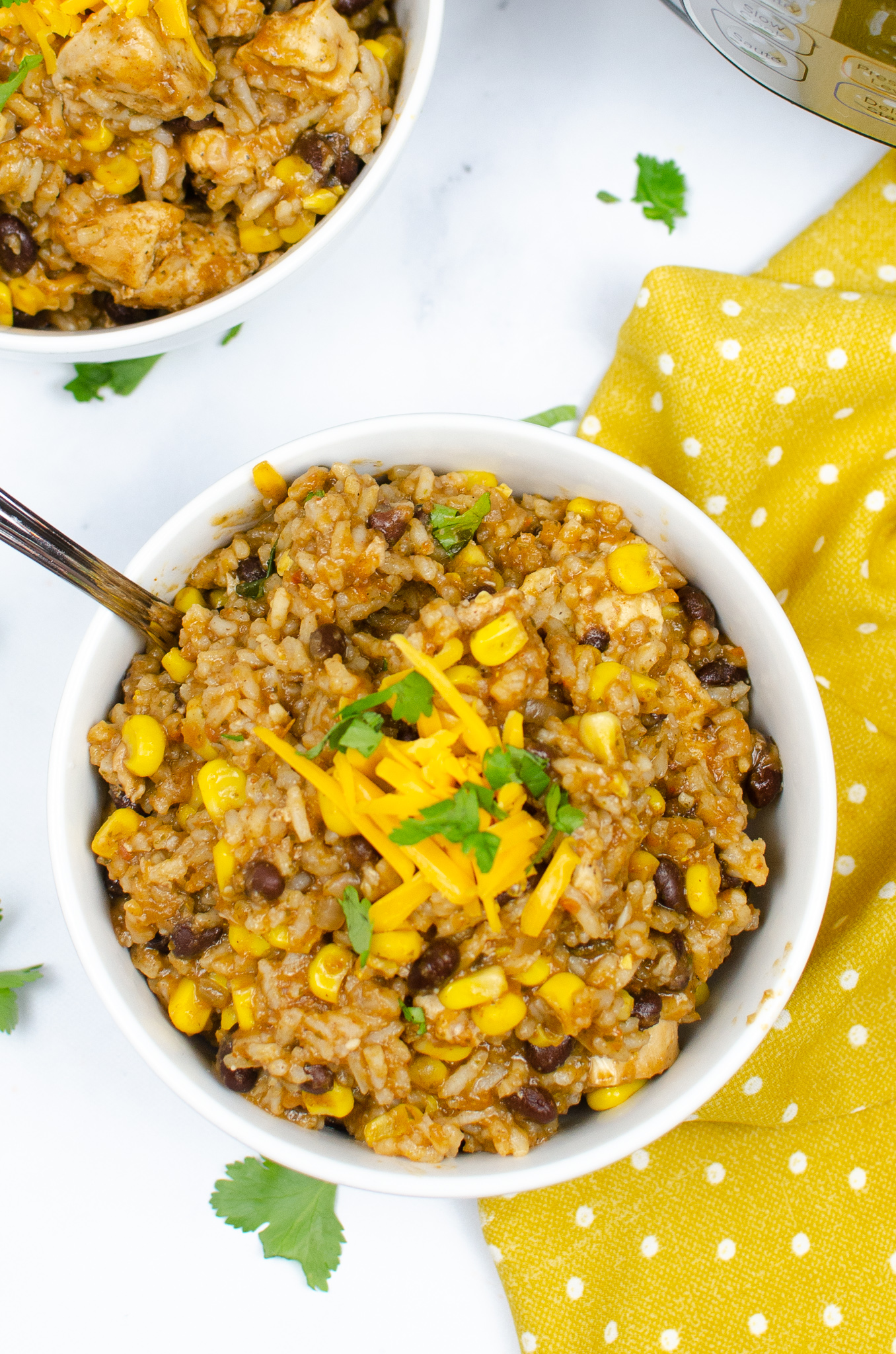 Two bowls of Instant Pot chicken burrito bowl topped with cheddar cheese and cilantro.