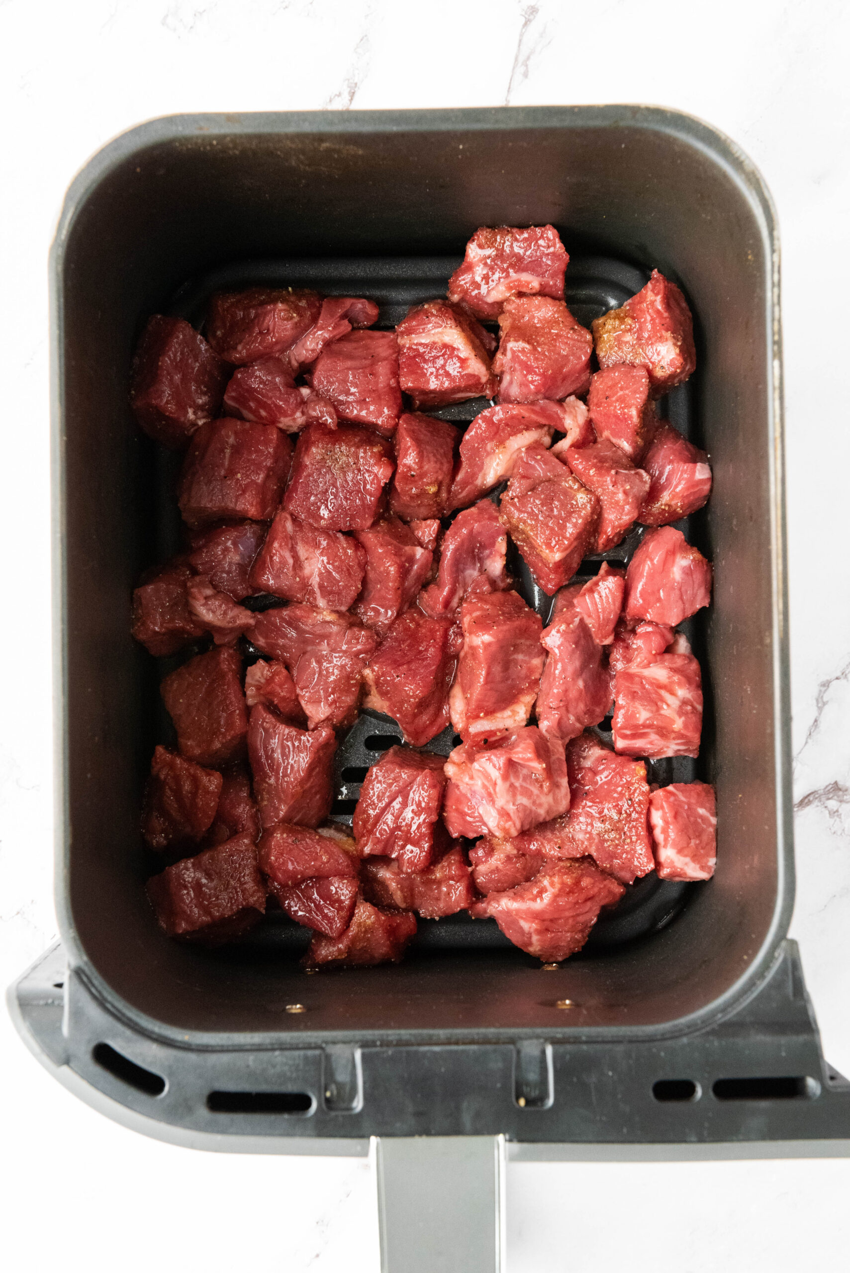 Marinated steak bites arranged in a single layer in an air fryer basket.