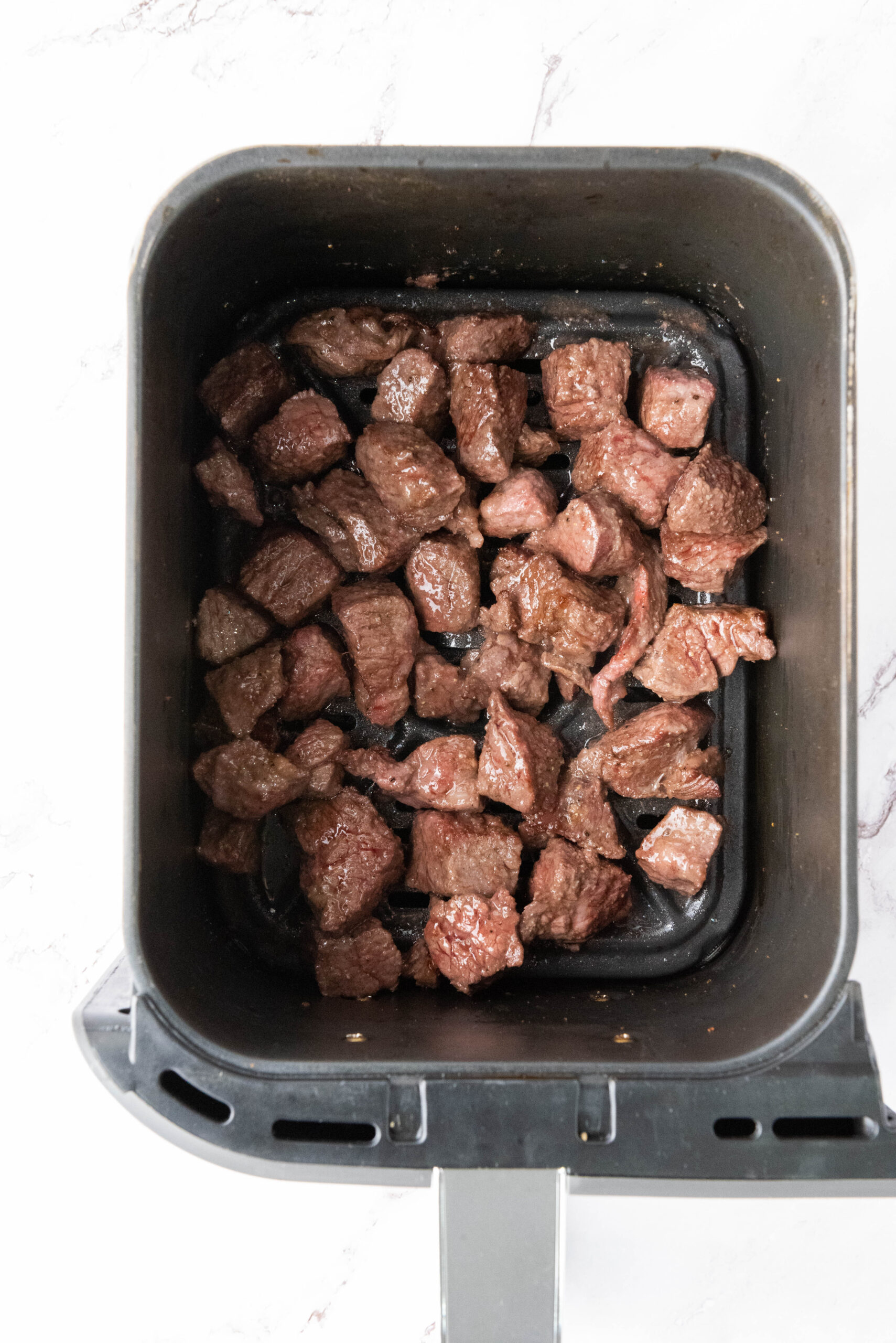 Browned steak bites cooked in an air fryer basket.