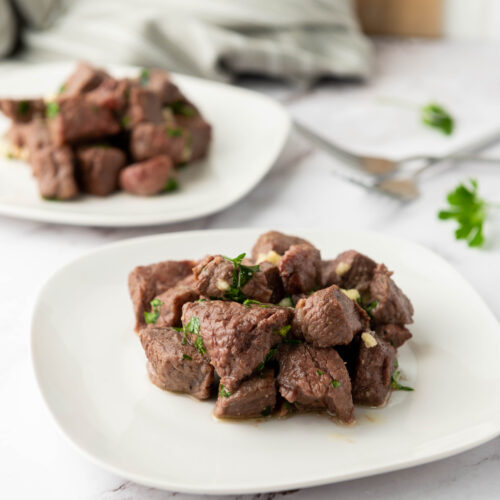 Garlic butter air fryer steak bites garnished with parsley on a white plate.