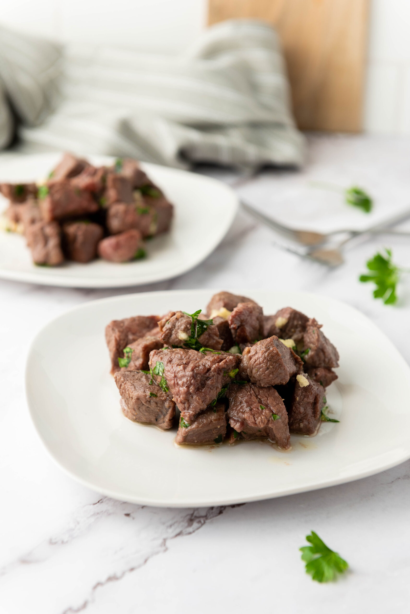 Garlic butter air fryer steak bites garnished with parsley on a white plate.