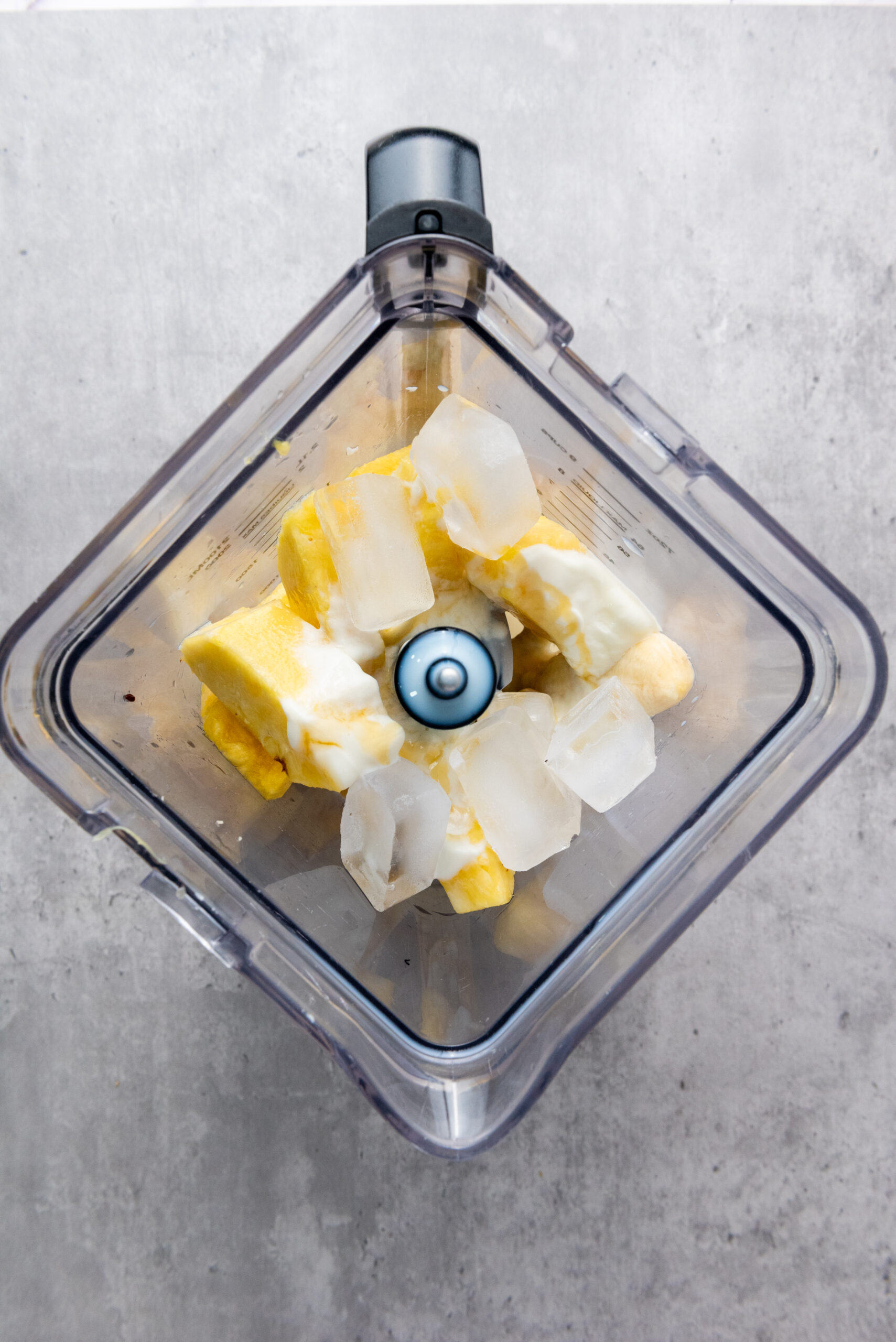 Ice cubes added to pineapple, banana, milk, Greek yogurt, and honey in a blender.