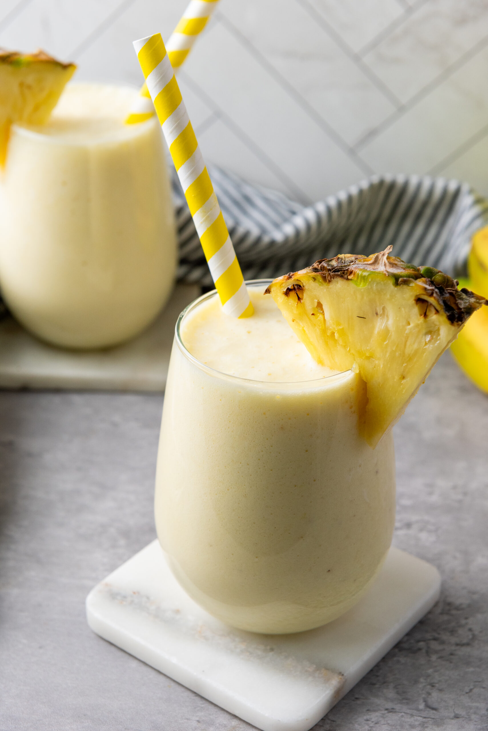 Creamy pineapple banana smoothie garnished with a pineapple wedge and striped straw.